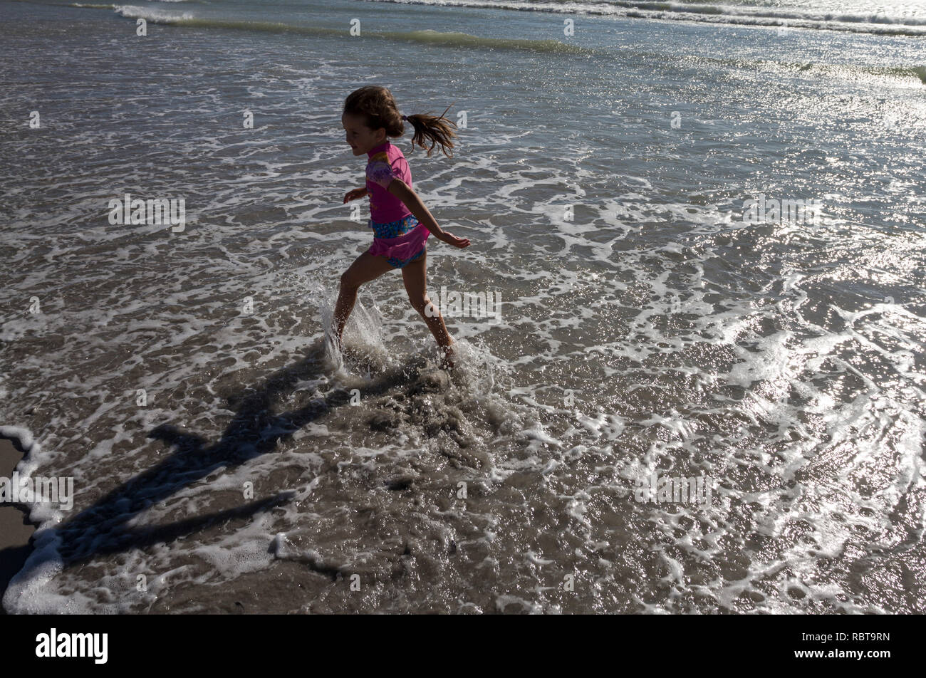 Young girl running in the shallow water on the beach in late afternoon sun Stock Photo