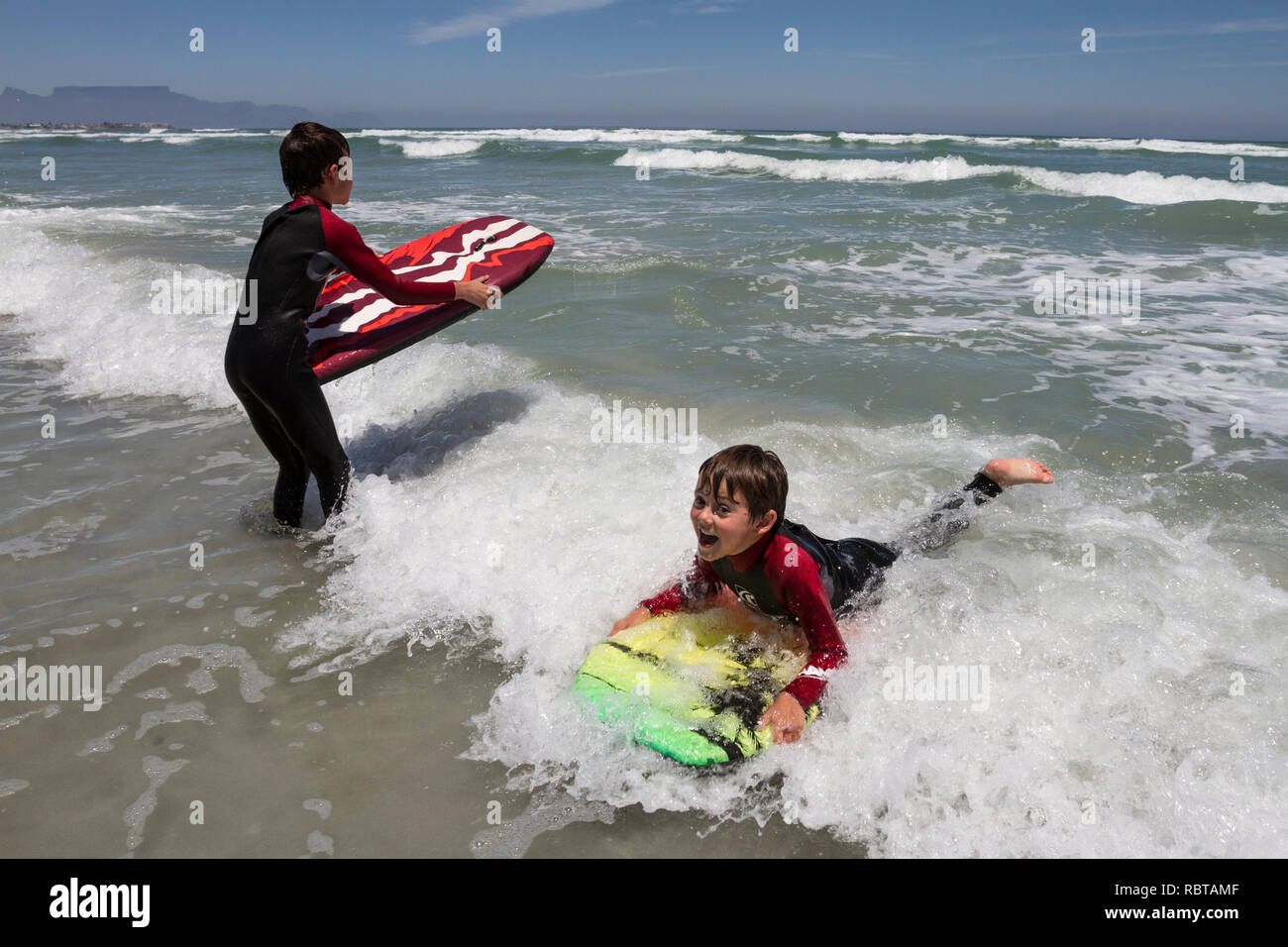 Young boys with boogy boards in the sea with Table Mountain in the background Stock Photo