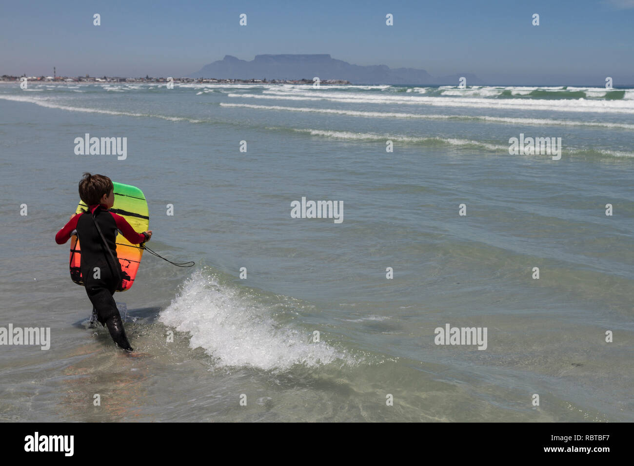 Young boy with boogy board in the sea with Table Mountain in the background Stock Photo