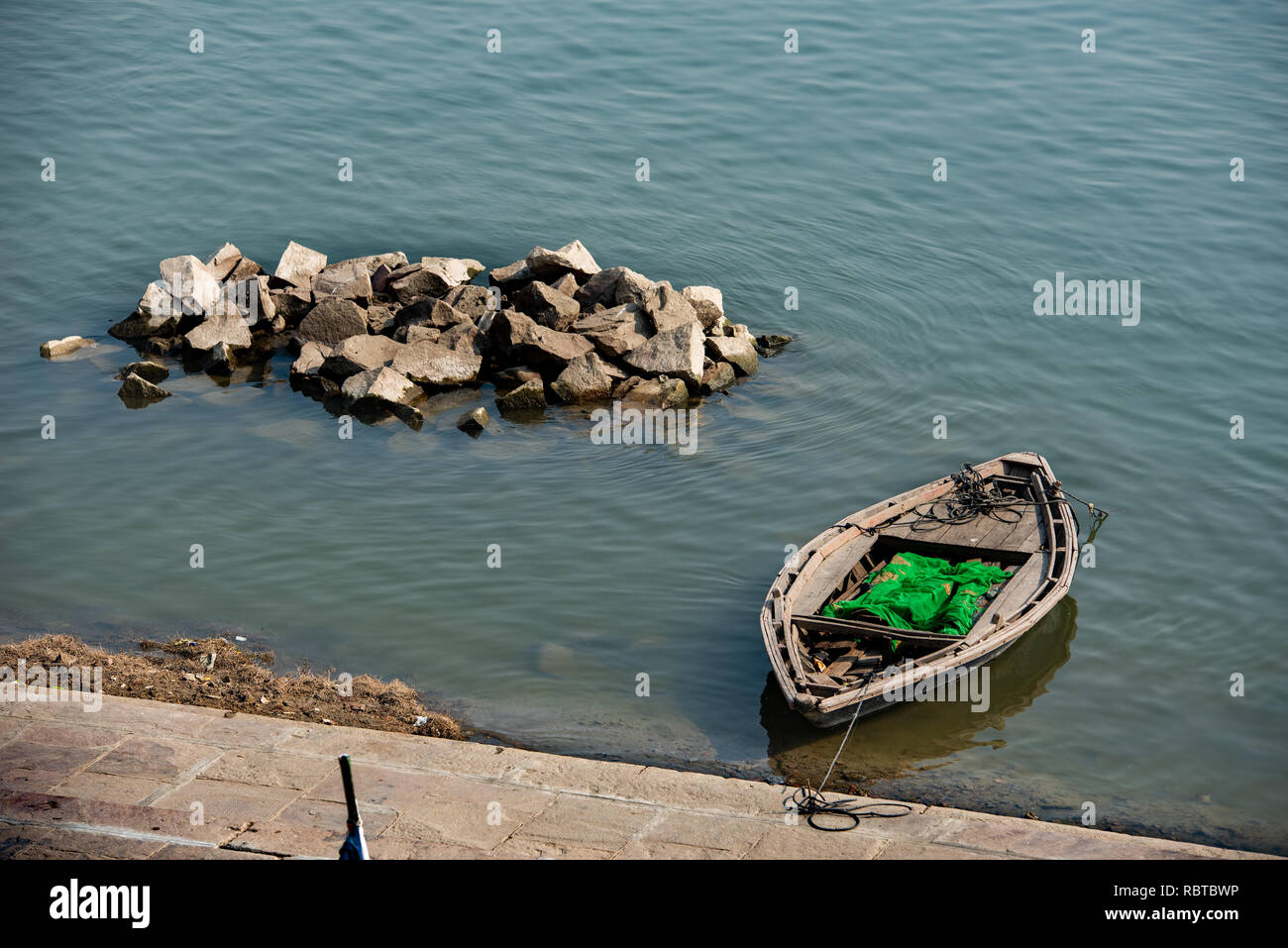 Composition with a moored boat  on the ghat and a pile of rocks in the Ganges in Varanasi, India. Stock Photo