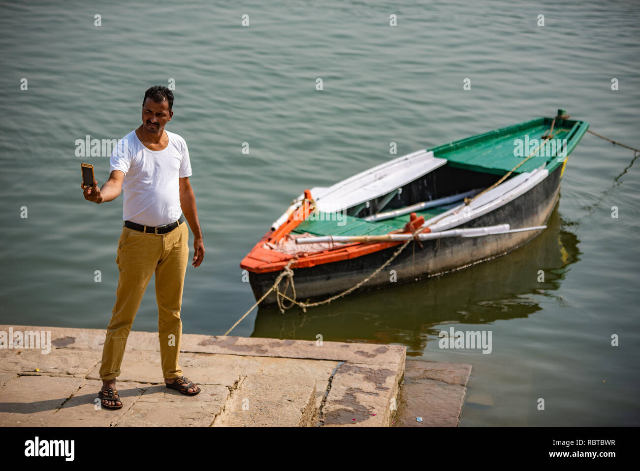 Man takes a patriotic selfie agains the backdrop of the Ganges with a single boat in the background; in Varanasi, India Stock Photo