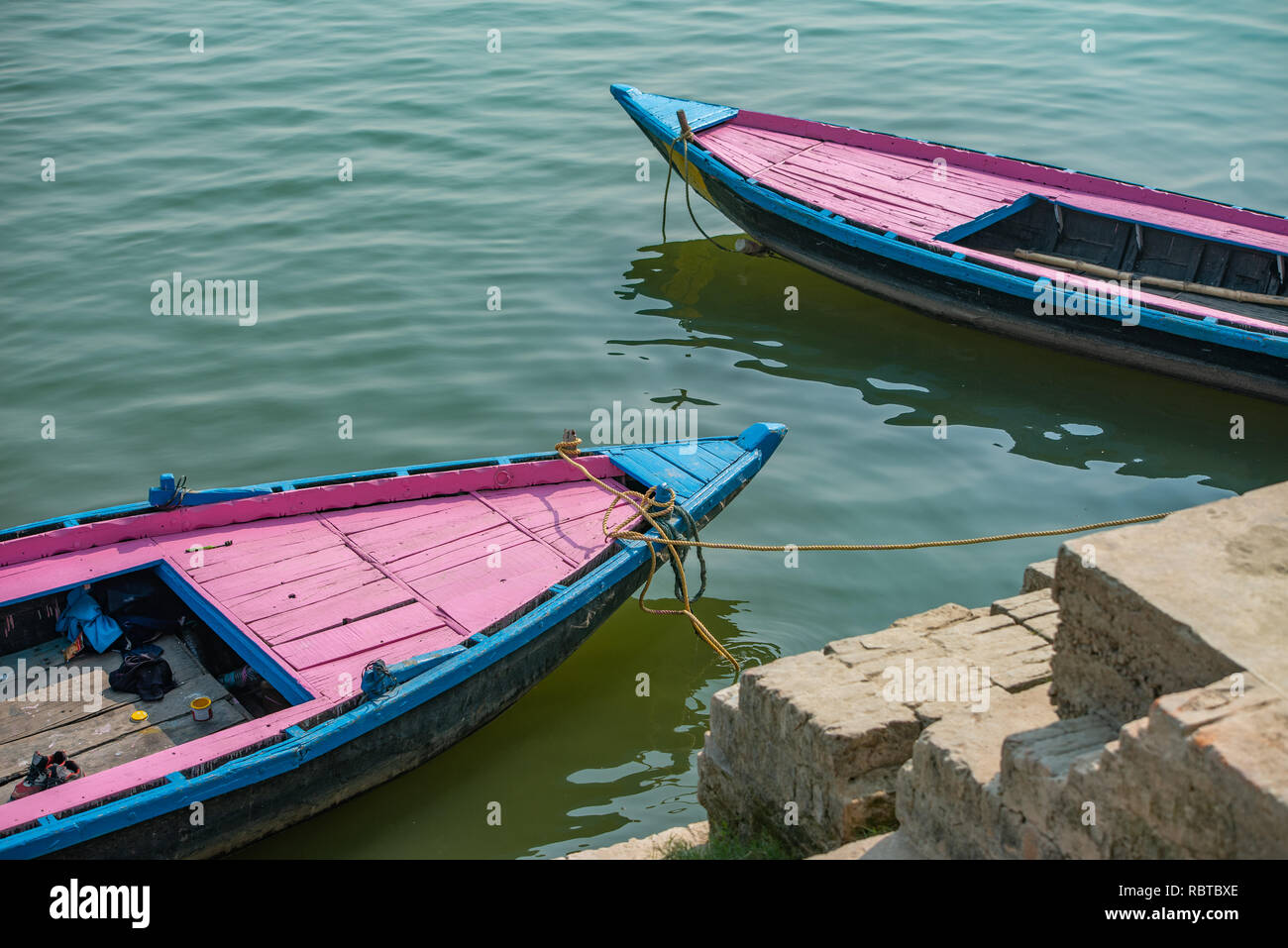Composition with pink and blue boats docked on the Ghat in Varanasi in India: The river's water provides a green backdrop for the two colourful boats. Stock Photo