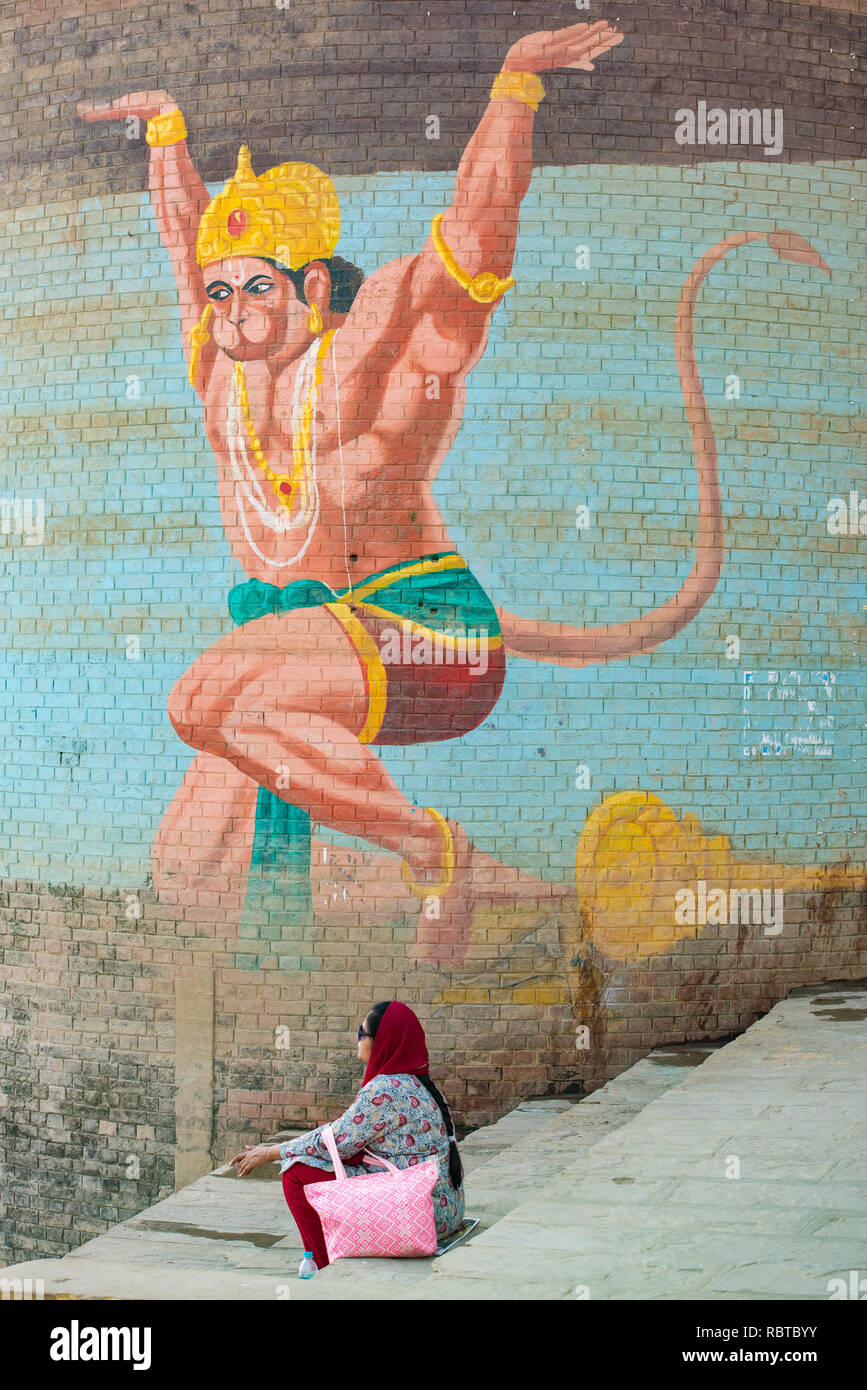 A wall mural painted on a water tank of the Hindu monkey god Hanuman with a woman sitting on the Ghat steps facing the Ganges in Varanasi, India Stock Photo