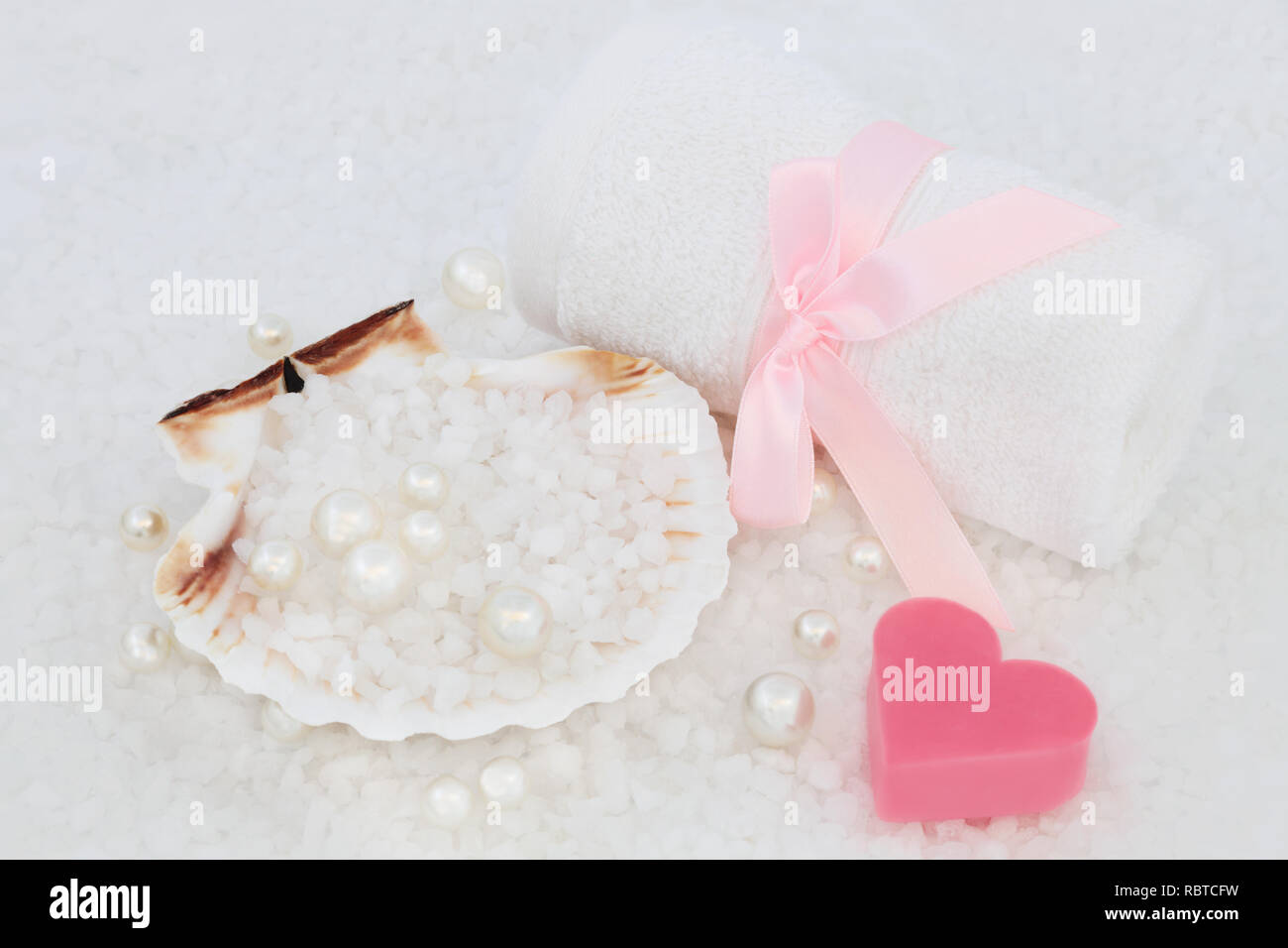Sea salt for skincare exfoliation beauty treatment in a scallop shell with white flannel, heart shaped soap and pearls. Health care concept, top view. Stock Photo