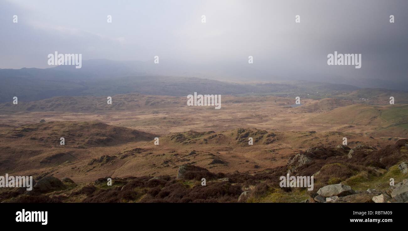 Rolling, broken moorland in North England (Lake District, Cumbria). Rocks, heather, bracken (brown). Dark clouds and mist on the hills in the distance Stock Photo