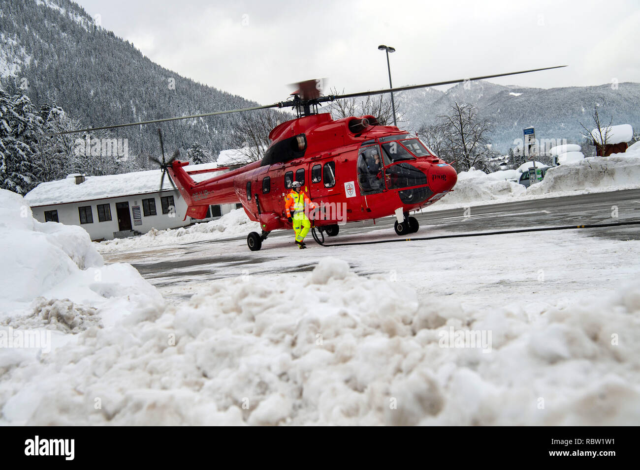 12 January 2019, Bavaria, Schönau Am Königssee: A helicopter of the type 'Super Puma' stands in a parking lot and is refuelled. The helicopter is supposed to whirl the snow from trees on roads and thus reduce the risk of branch breakage. The heavy snowfalls of the past few days continue to keep the emergency forces in suspense in southern Bavaria and new snow is already approaching. According to the authorities, more than 1000 helpers have been deployed in the southern districts of Upper Bavaria. Photo: Lino Mirgeler/dpa Stock Photo