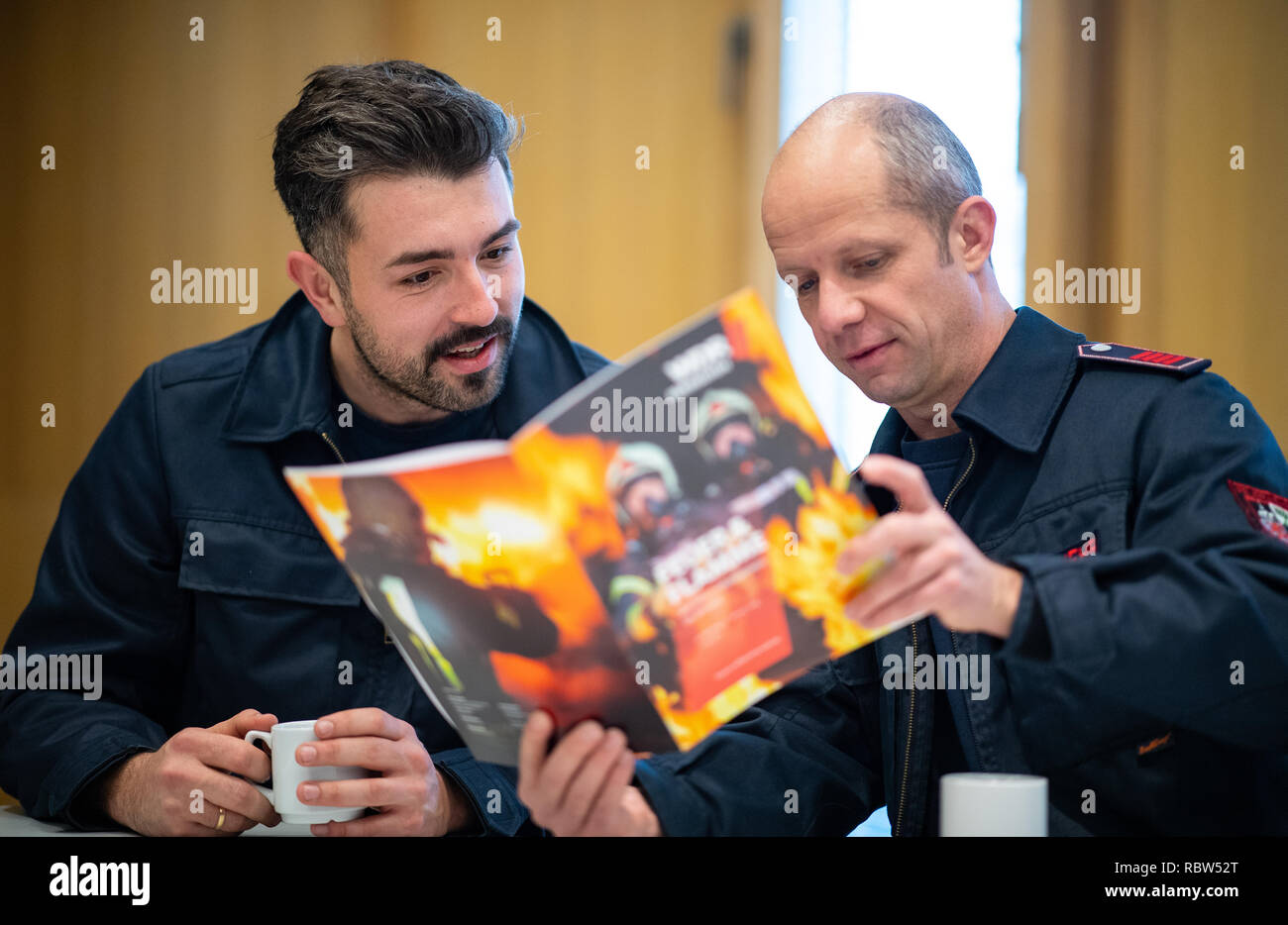 10 January 2019, North Rhine-Westphalia, Gelsenkirchen: The firemen Philip (l) and Hacki sit in the lounge of the fire station in Gelsenkirchen and browse through the WDR magazine of the Feuer & Flamme series. After the great success of the first season, which ran on WDR television in mid-2017 and was nominated for the German Television Prize, the documentary series will be continued on WDR television from 21 January to 25 March 2019, Monday from 8.15 p.m. The production effort was enormous: 70 days in a row, 24 hours a day the 20-man TV crew shot. During the missions, up to 57 special cameras Stock Photo