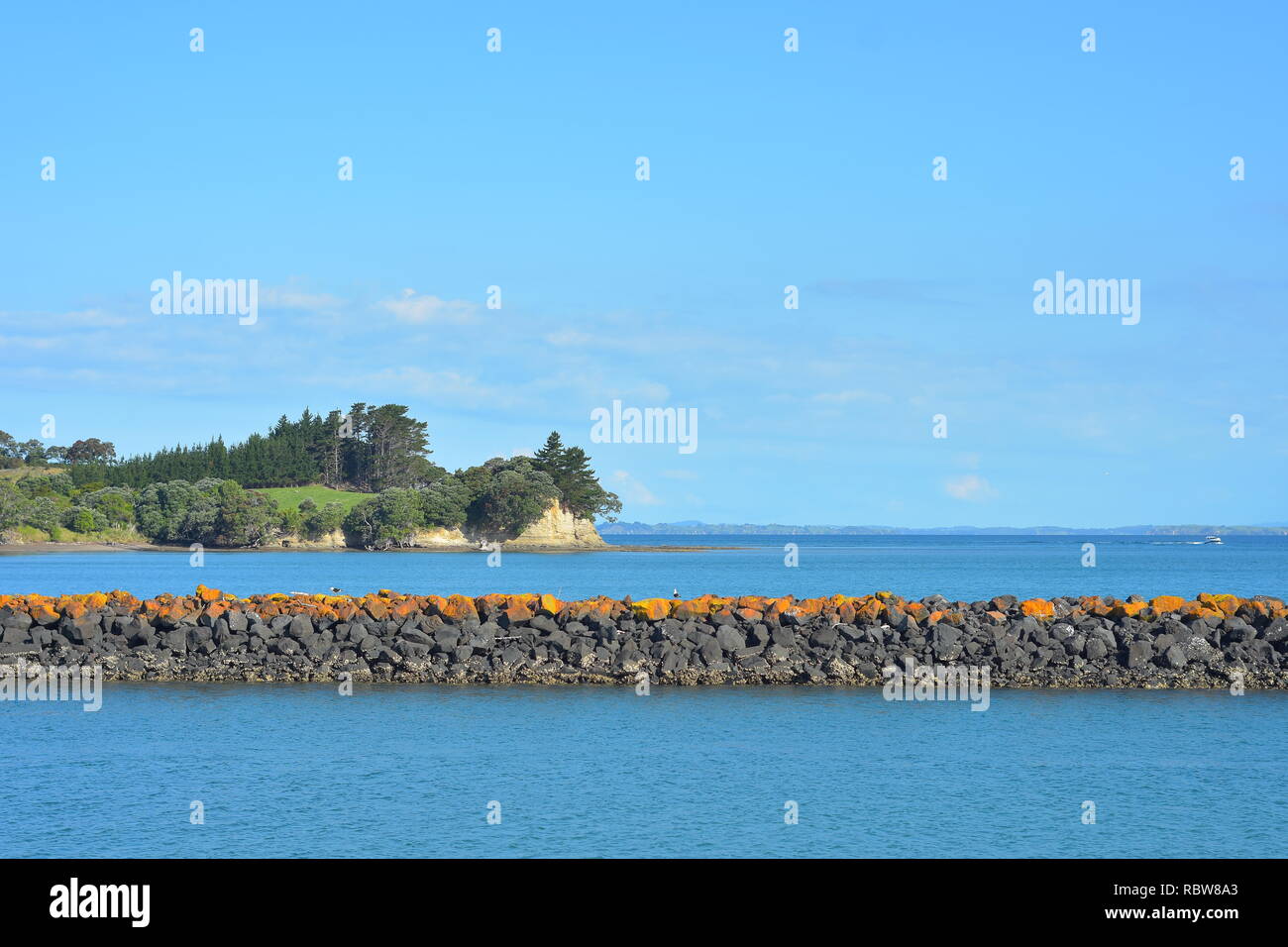 Sea wall made of free laid cut stone in blue sea on sunny day. Note bright yellow lichen growth on top of wall indicating areas where high tide water  Stock Photo