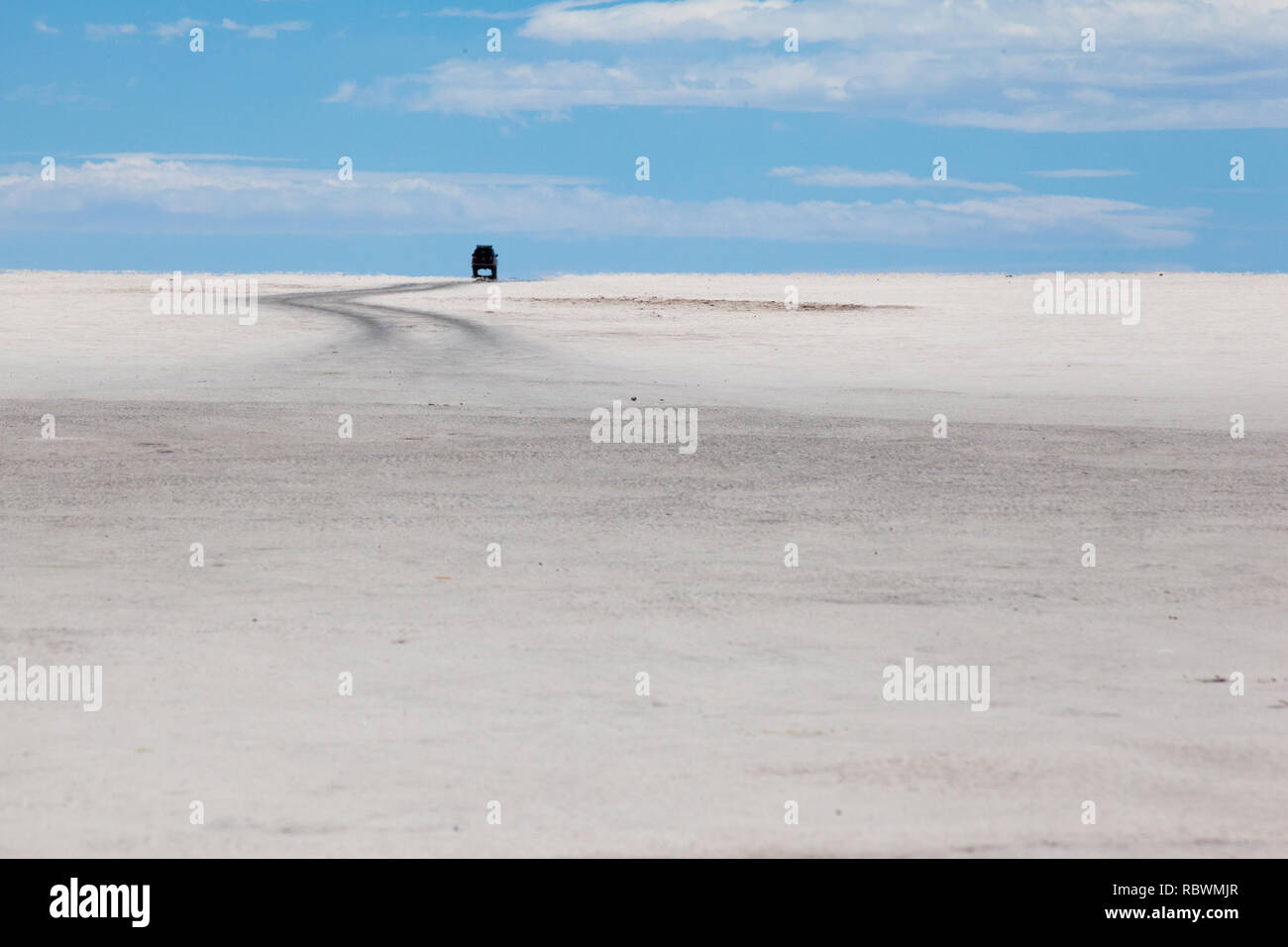 A four wheel drive (4WD) tour across the salt plains of Uyuni follows a road to the horizon. Stock Photo