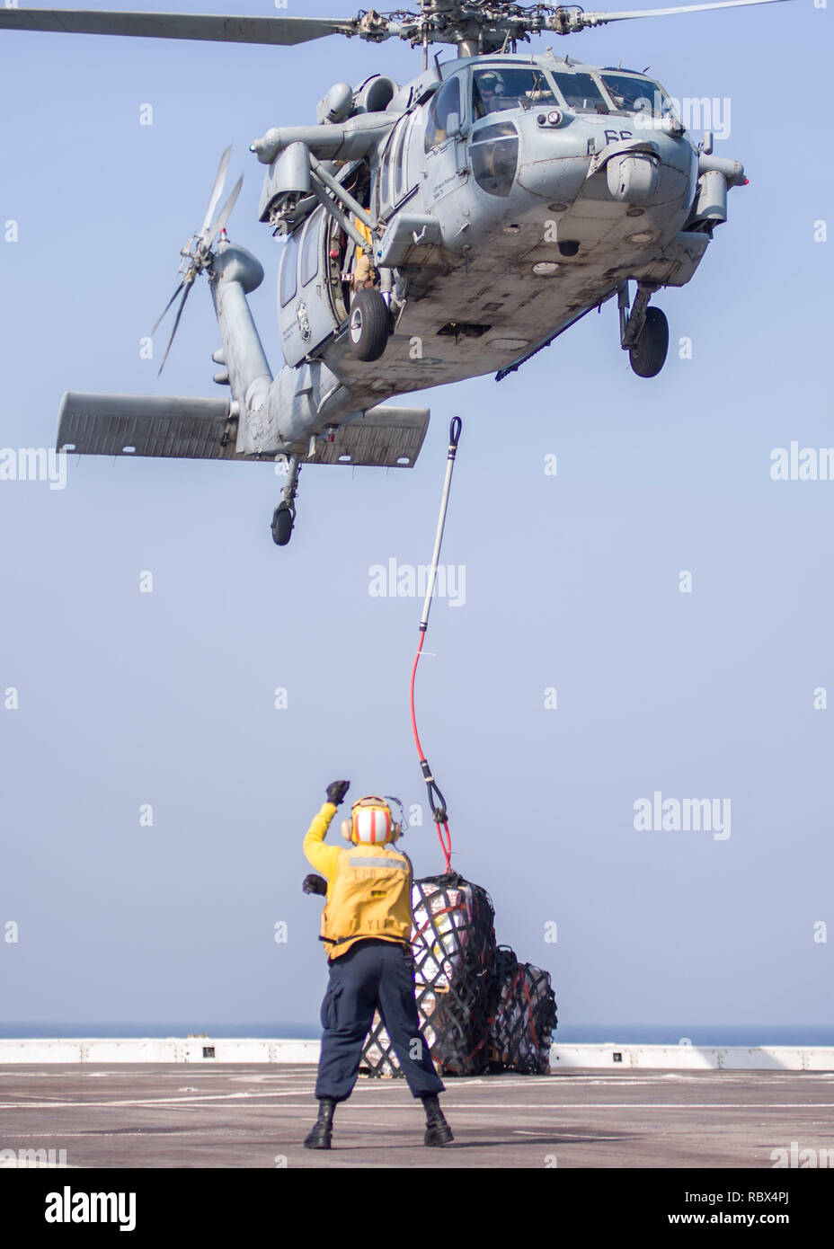 190107-N-PH222-1349 ARABIAN SEA (Jan. 7, 2018) Aviation Boatswain’s Mate (Handling) 2nd Class Brittany Brown, from Fort Lauderdale, Fla., assigned to the San Antonio-class amphibious transport dock ship USS Anchorage (LPD 23), signals a MH-60S Sea Hawk helicopter, attached to the “Blackjacks” of Helicopter Sea Combat Squadron (HSC) 21, during a vertical replenishment while on a deployment of the Essex Amphibious Ready Group (ARG) and 13th Marine Expeditionary Unit (MEU). The Essex ARG/13th MEU is flexible and persistent Navy-Marine Corps team deployed to the U.S. 5th Fleet area of operations i Stock Photo