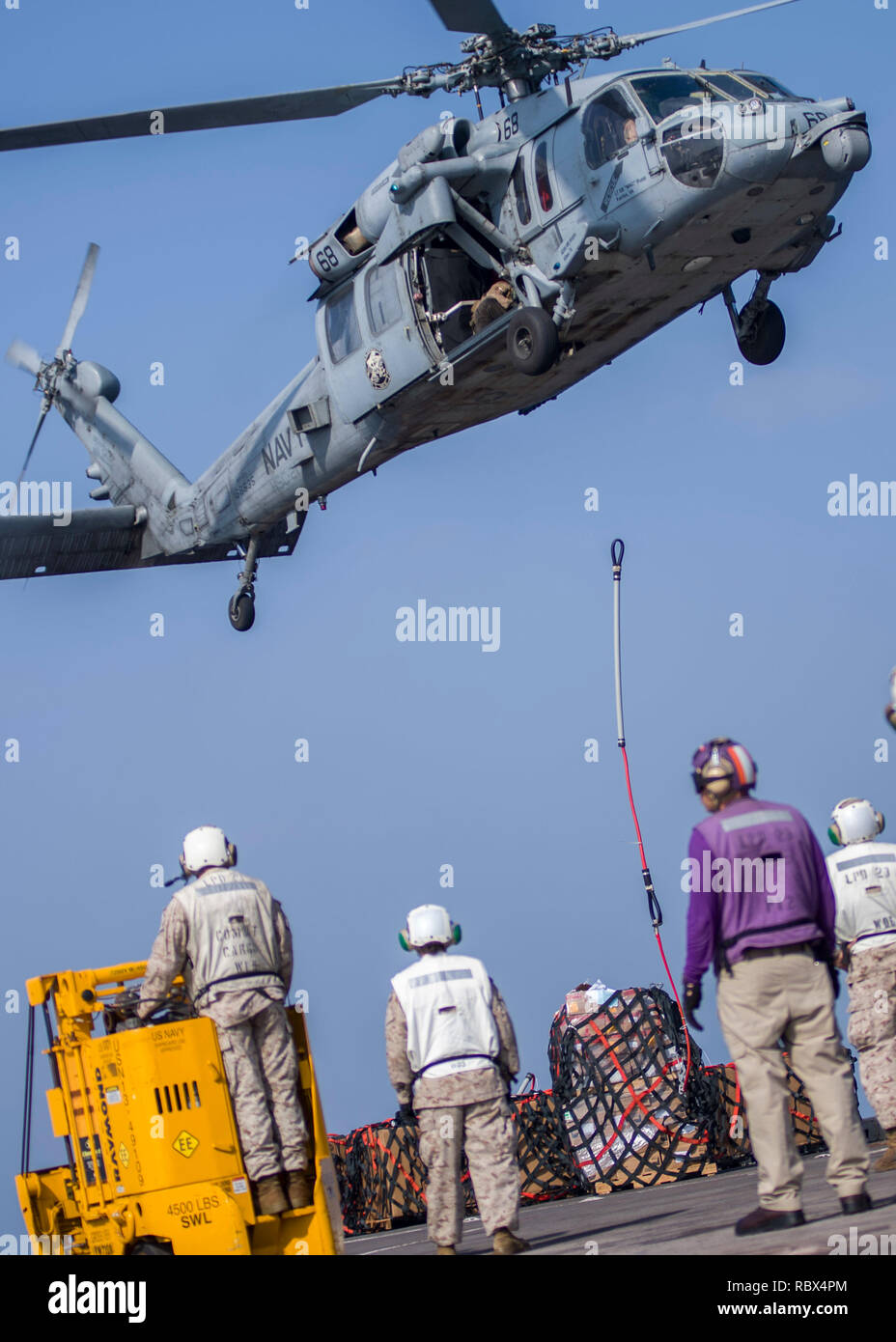 190107-N-PH222-1386 ARABIAN SEA (Jan. 7, 2018) Marines assigned to the 13th Marine Expeditionary Unit (MEU) and Sailors assigned to the San Antonio-class amphibious transport dock ship USS Anchorage (LPD 23) prepare to recover cargo delivered from an MH-60S Sea Hawk helicopter attached to Helicopter Sea Combat Squadron (HSC) 21, during a vertical replenishment while on a deployment of the Essex Amphibious Ready Group (ARG) and 13th MEU. The Essex ARG/13th MEU is flexible and persistent Navy-Marine Corps team deployed to the U.S. 5th Fleet area of operations in support of naval operations to en Stock Photo