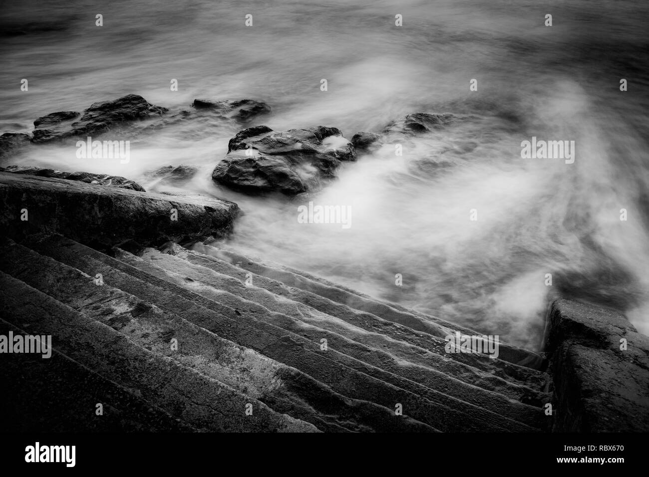 The tide washing up against steps on the seafront slow shutter speed Stock Photo