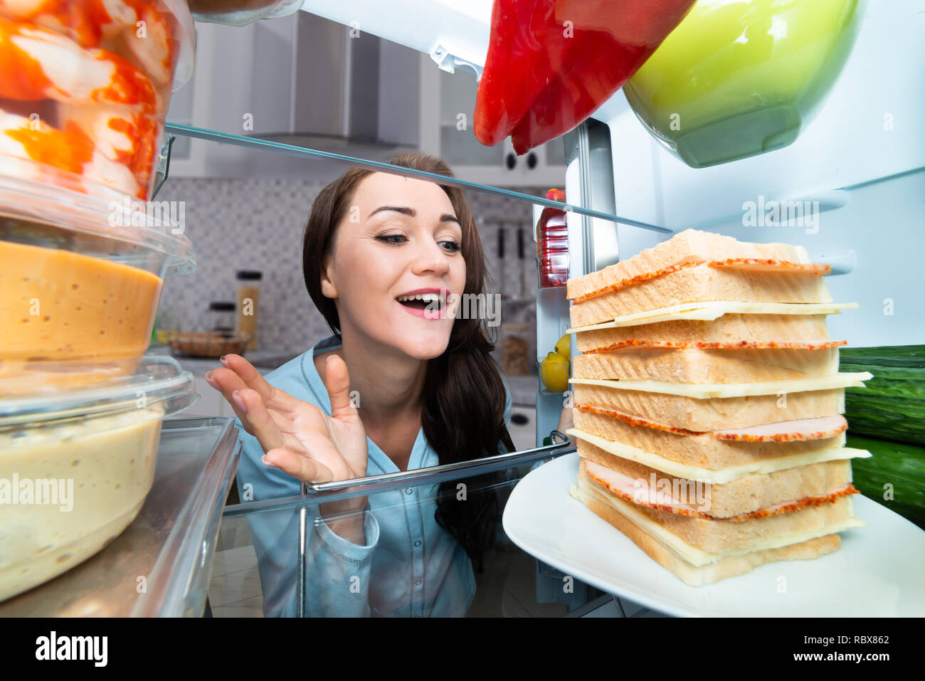 Hungry Woman Looking At Sandwich In An Open Refrigerator Stock Photo