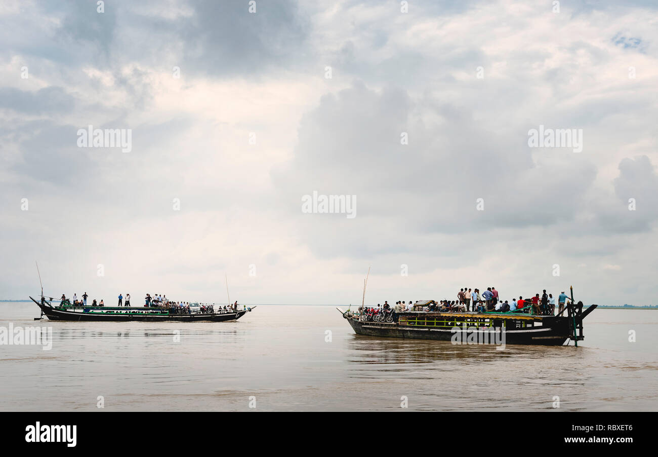 Public ferries over-loaded with passengers, motorcycles, and cars cross the Brahmaputra river in flood during monsoon season, Jorhat, Assam, India. Stock Photo