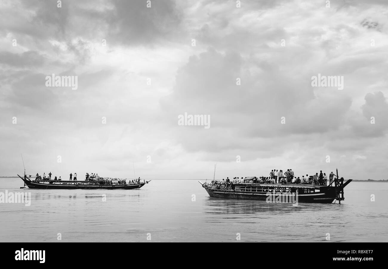 Public ferries over-loaded with passengers, motorcycles, and cars cross the Brahmaputra river in flood during monsoon season, Jorhat, Assam, India. Stock Photo