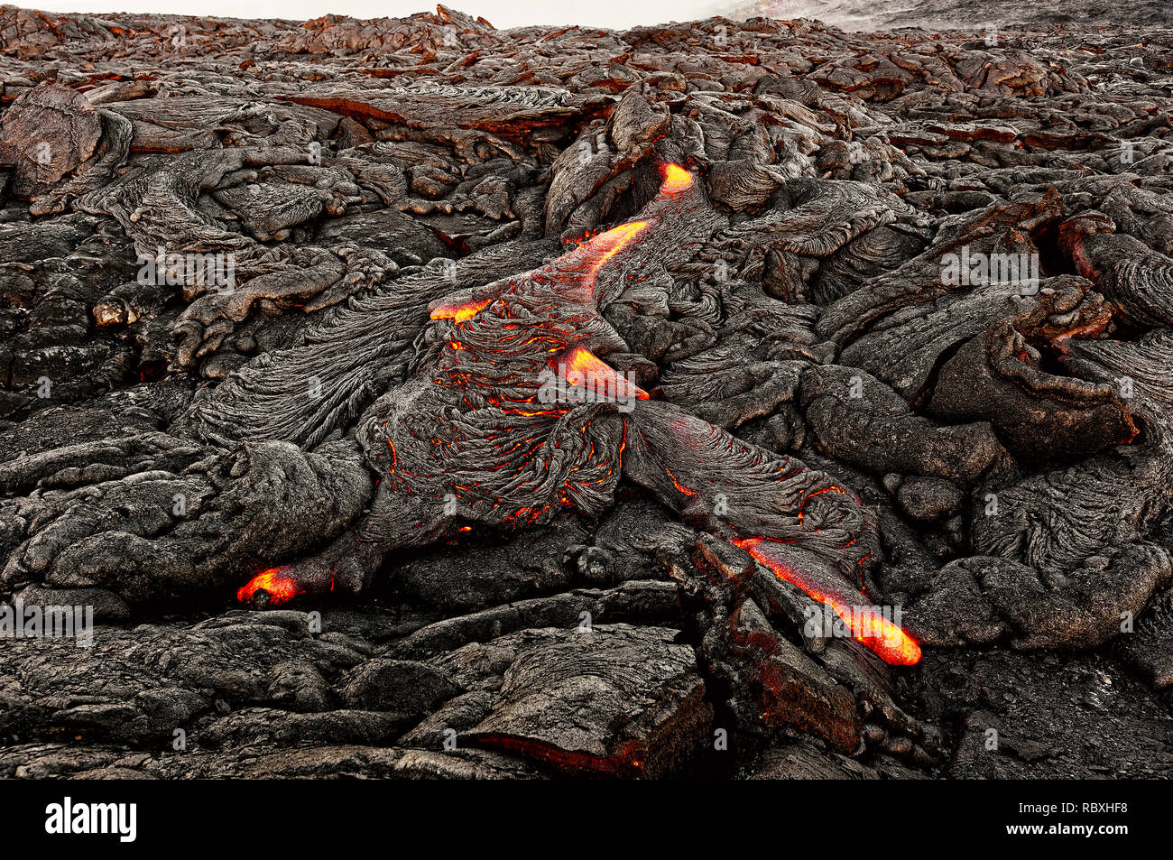 A lava flow emerges from an earth column and flows in a black volcanic landscape, in the sky shows the first daylight - Location: Hawaii, Big Island,  Stock Photo