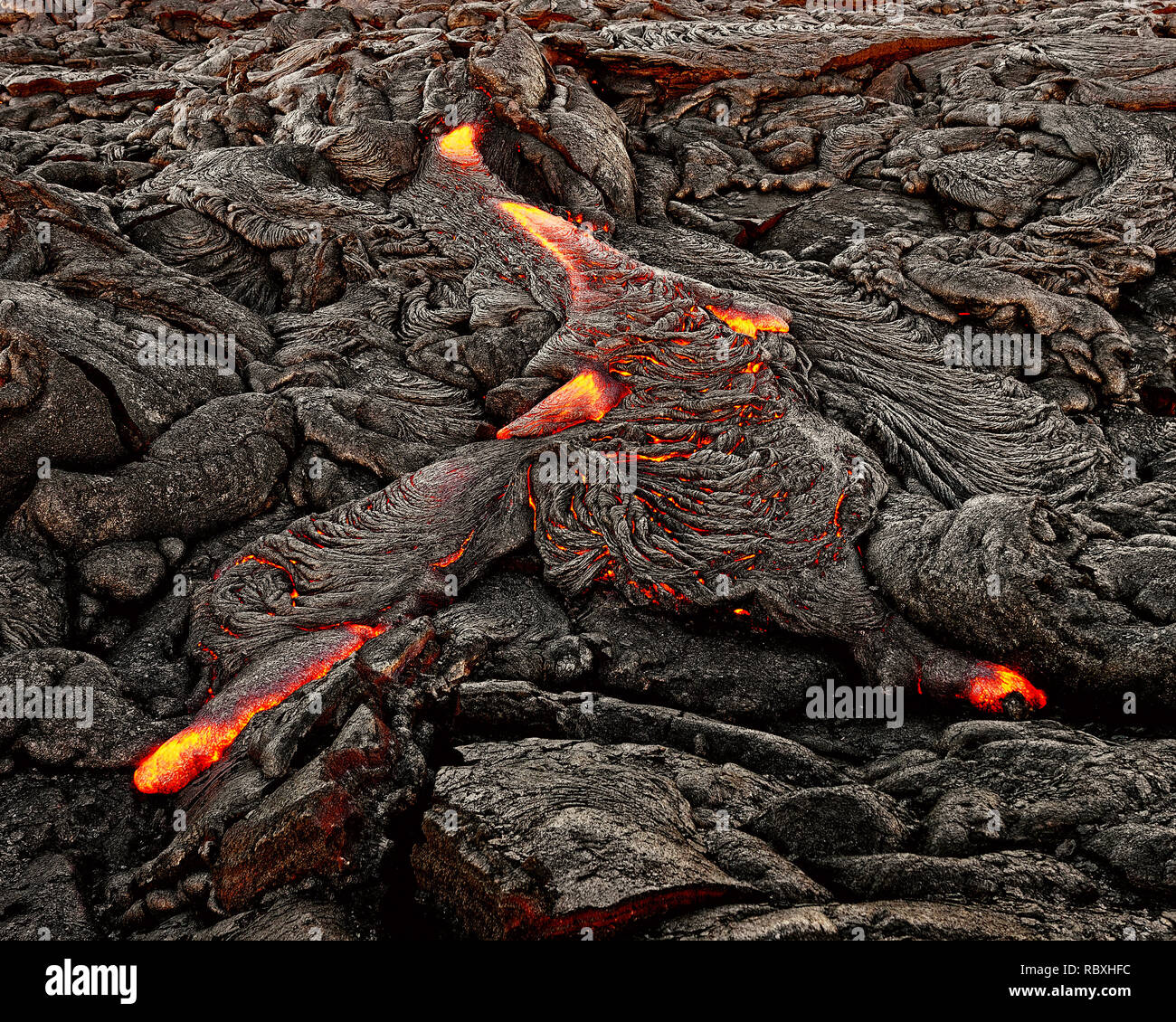A lava flow emerges from an earth crevice and flows in a black volcanic landscape, glowing magma, first daylight - Location: Hawaii, Big Island, volca Stock Photo