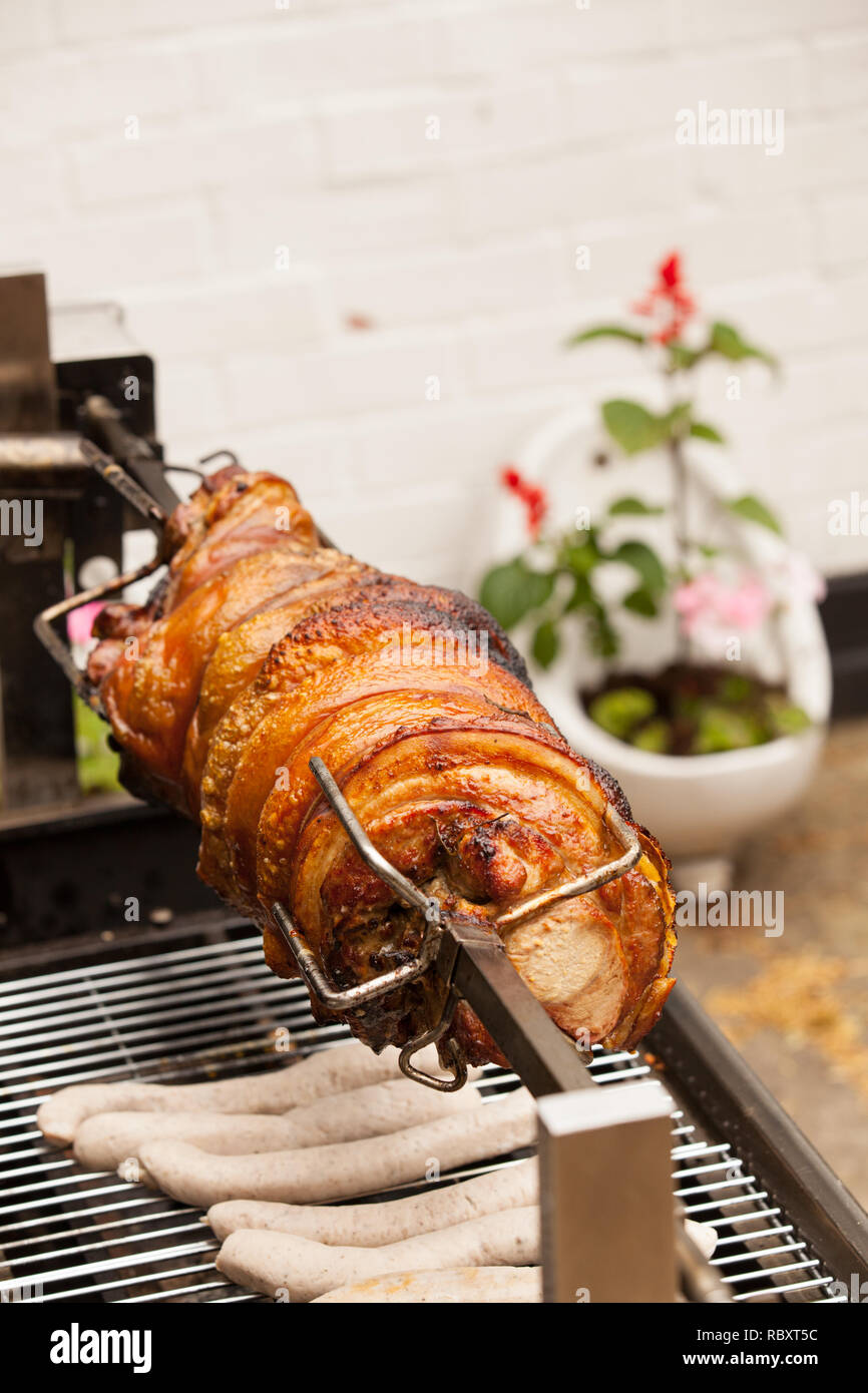 Pork spit roast at Pub in England.  Flower planted old urinal in background Stock Photo
