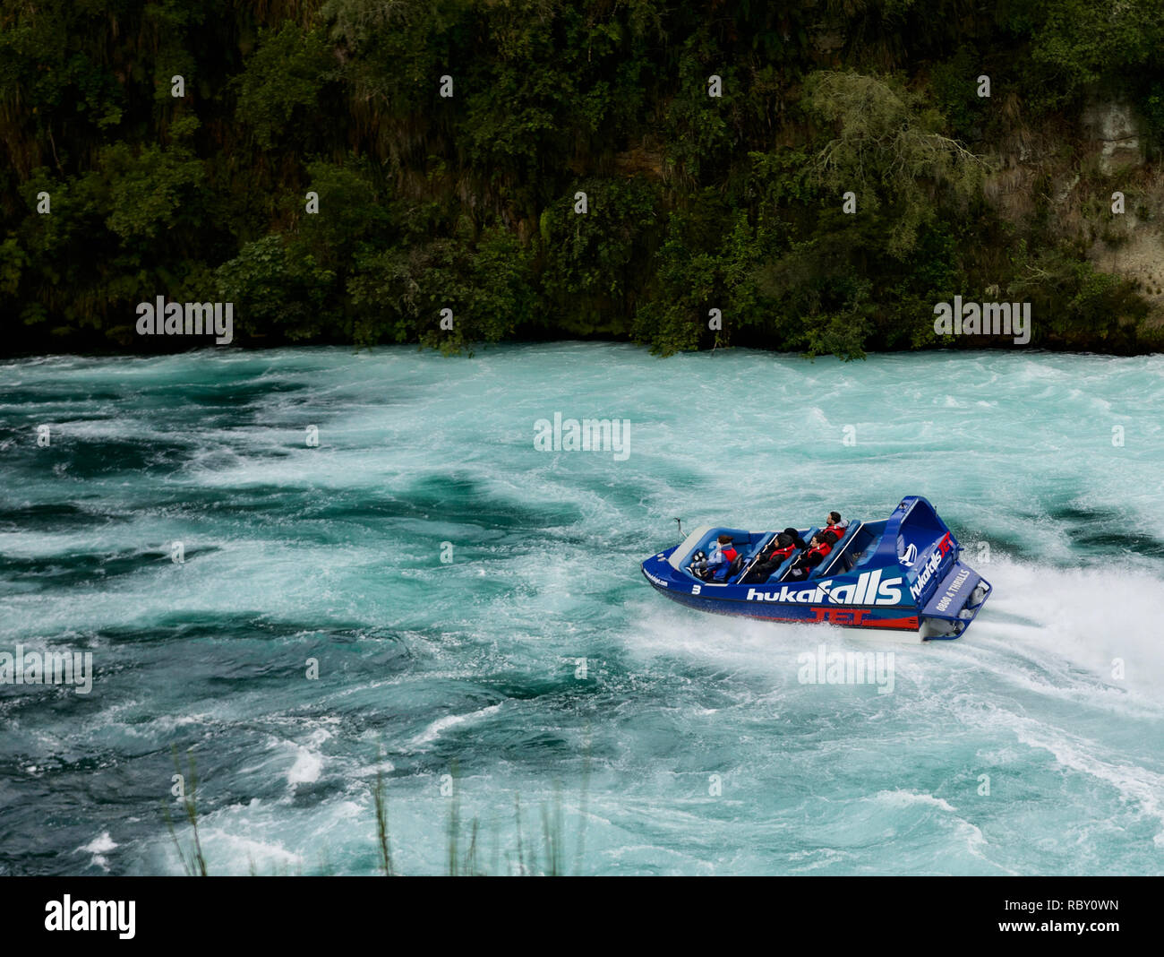 Huka Falls Jet boat leaving the falls behind in deep blue and white turbulent waters Stock Photo