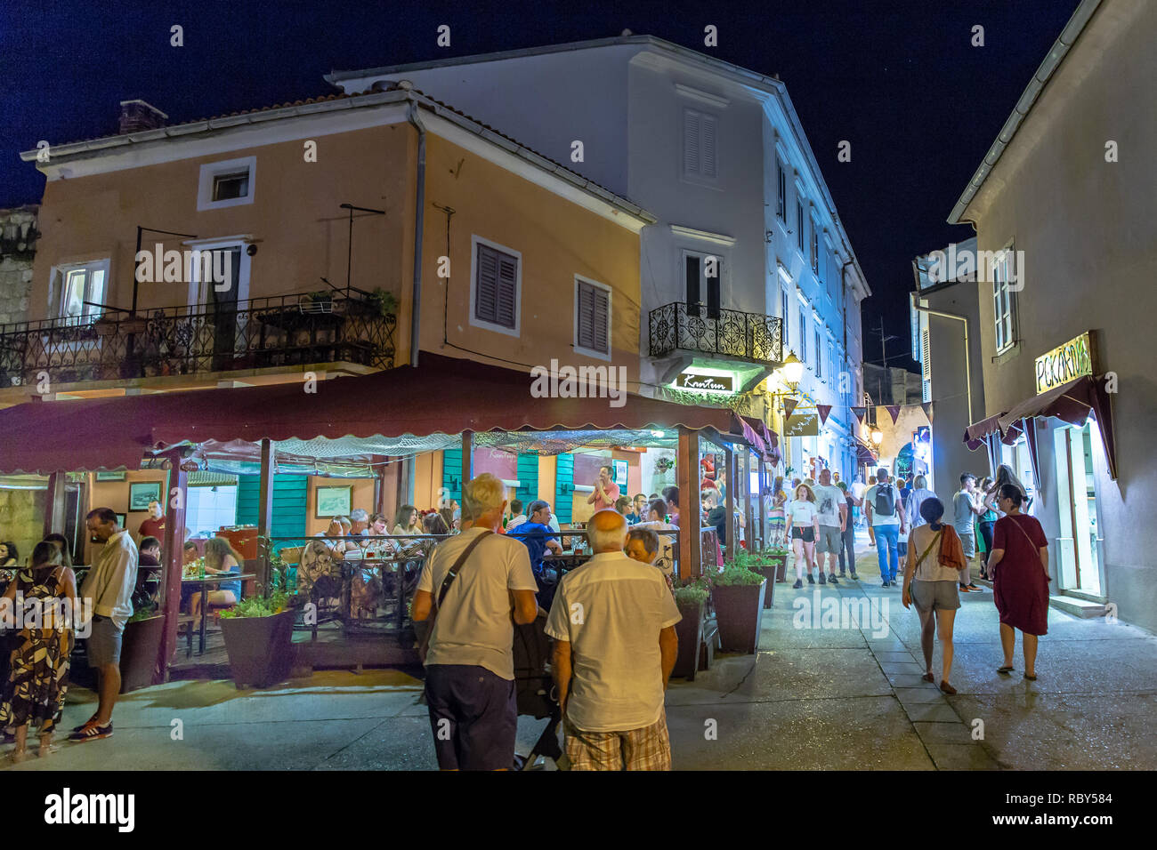 Tourists dine outdoors in the evening in a restaurantat at the head of a traditional narrow street in Krk, Kvarner, Croatia. Stock Photo