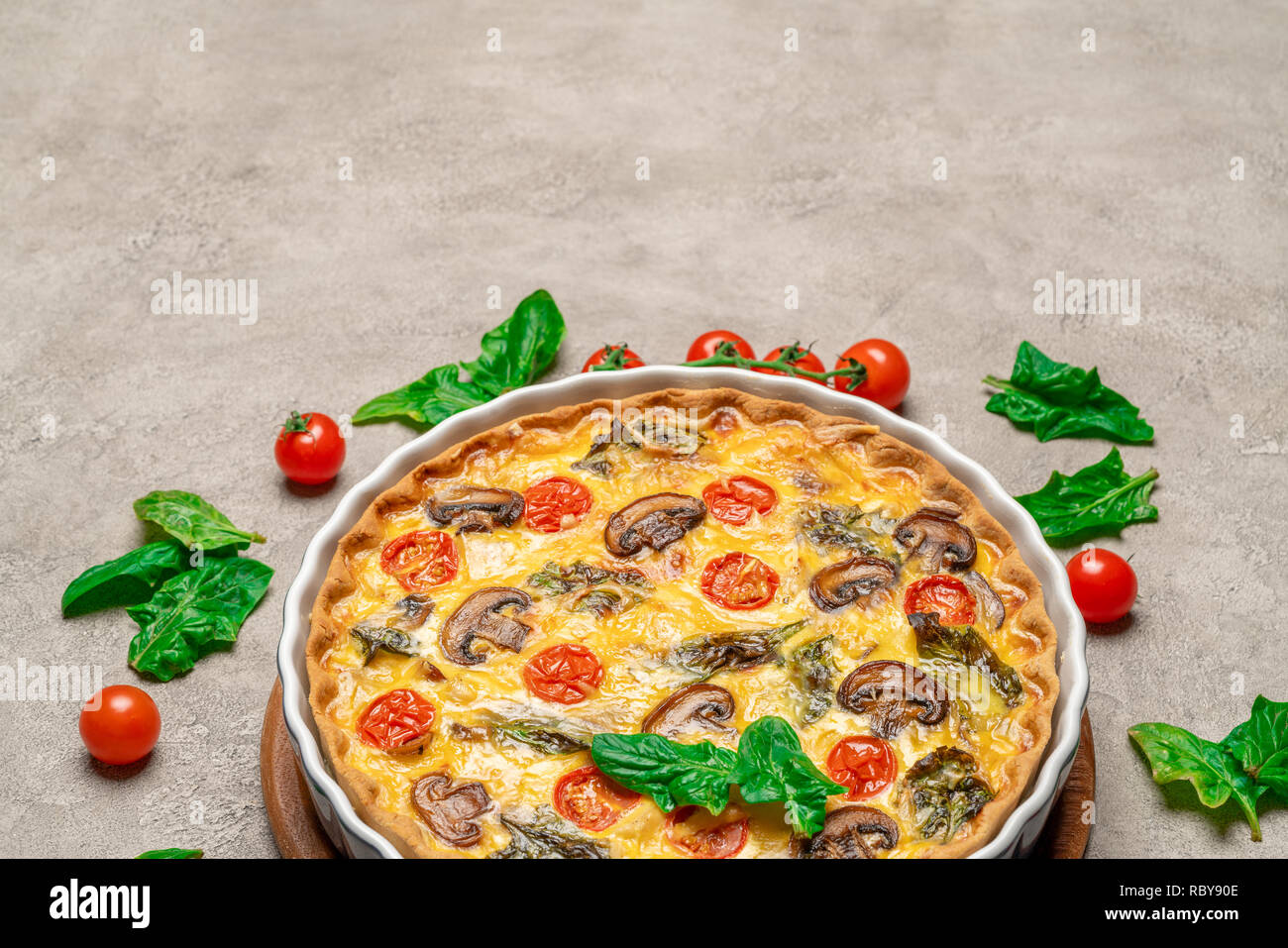 Baked homemade quiche pie in ceramic baking form on concrete background