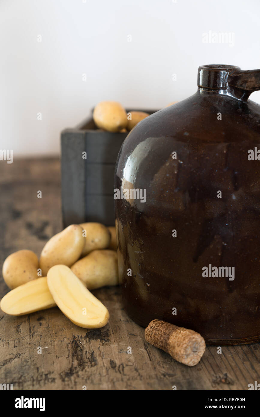 vintage moonshine jug on a rustic wooden table with potatoes and corn cob cork for distilling hard liquor Stock Photo