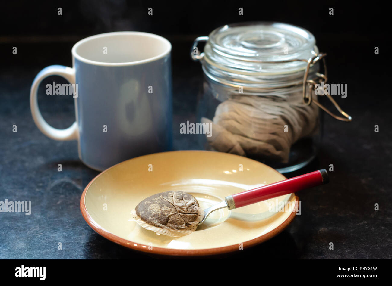 A blue mug, a jar of tea bags a saucer, teaspoon and used tea bag on a