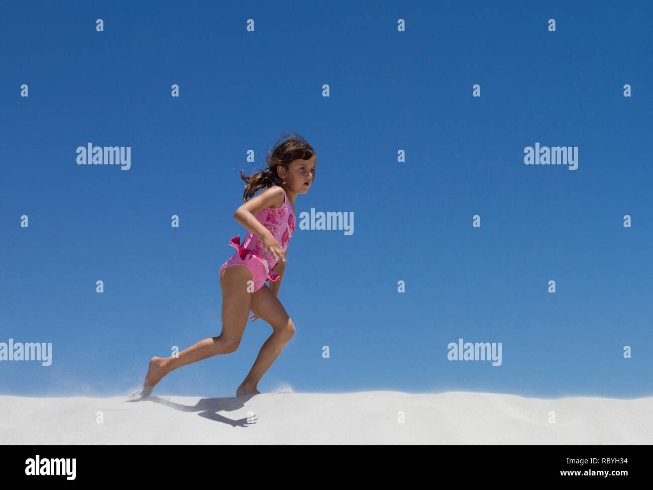 Young girl in pink swimming costume runs on a sand dune on the beach Stock Photo