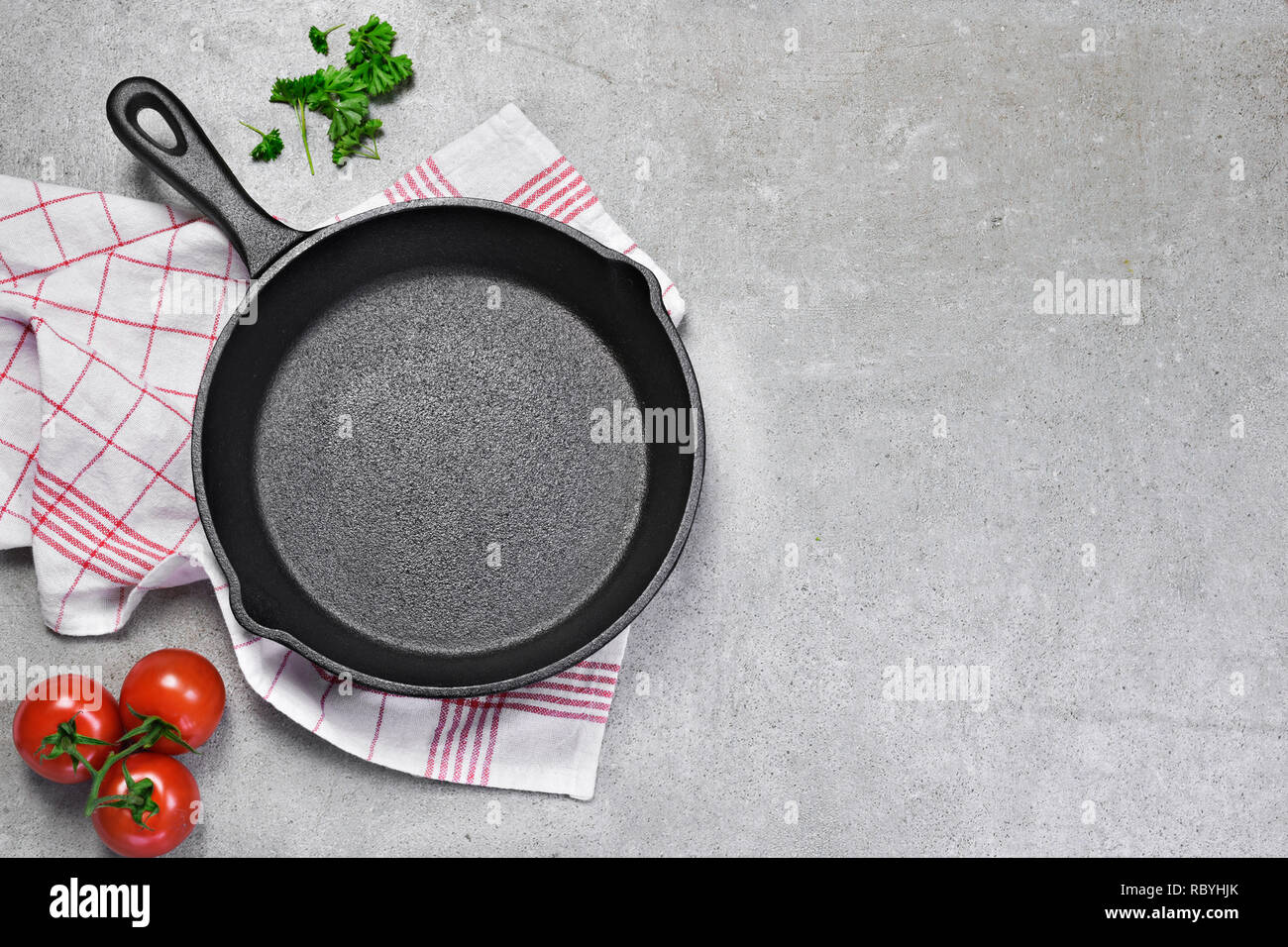 Cast iron pan on a grunge concrete background with copy space. Empty iron pan, top view or high angle shot with herbs and tomatoes.Cast iron pan on a Stock Photo