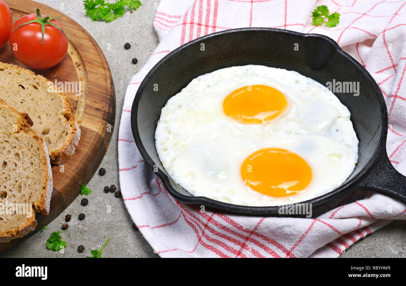 Delicious fried eggs in a cast iron pan. Top view of eggs and bread, breakfast scene. Stock Photo