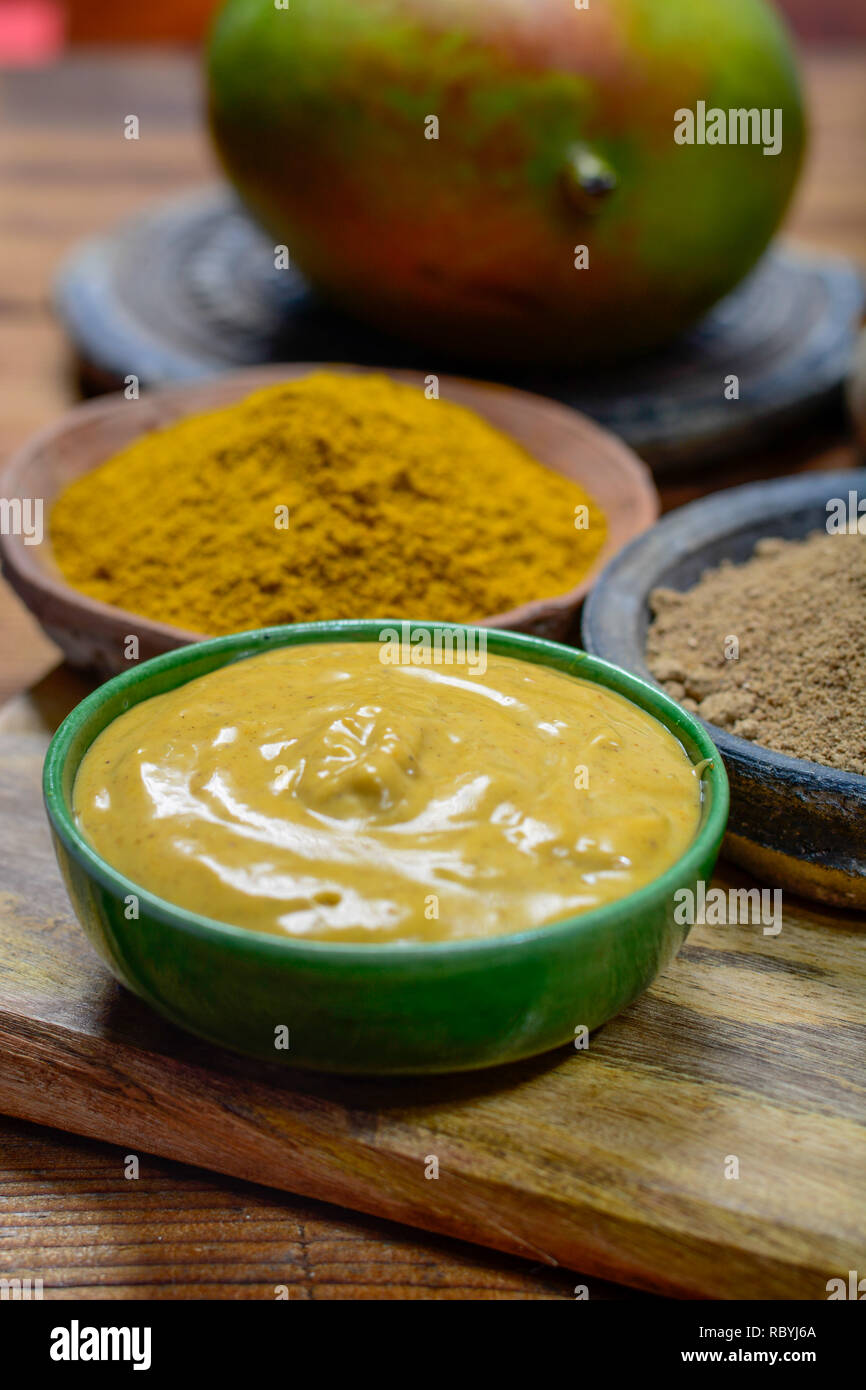 Tasty mango-curry sauce in small bowl ready to eat and bowls with mango and curry powder close- up Stock Photo