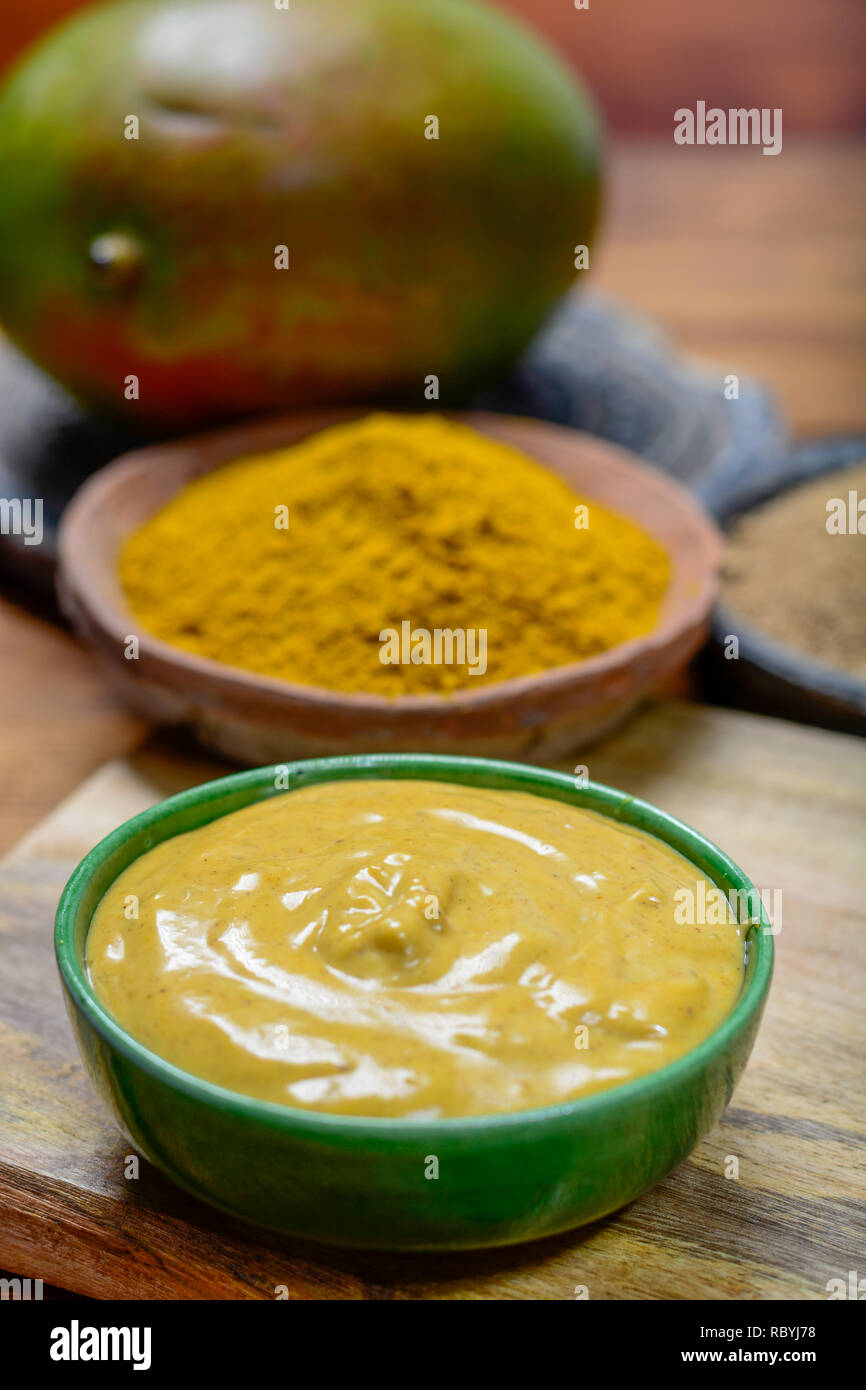 Tasty mango-curry sauce in small bowl ready to eat and bowls with mango and curry powder close- up Stock Photo