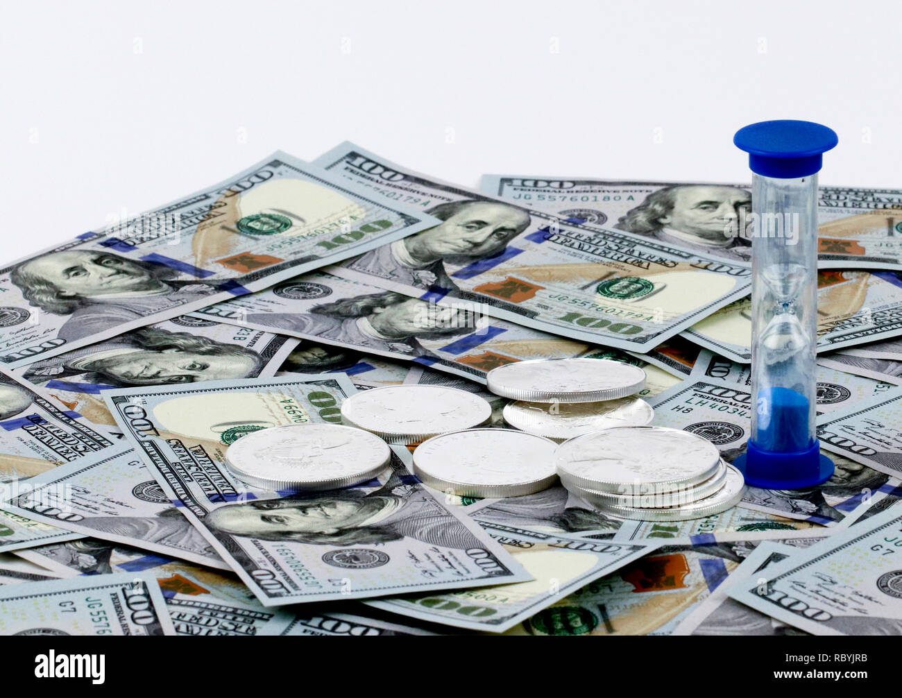 Timer on a layer of 100 Dollar bills and a stack of silver with a white background Stock Photo