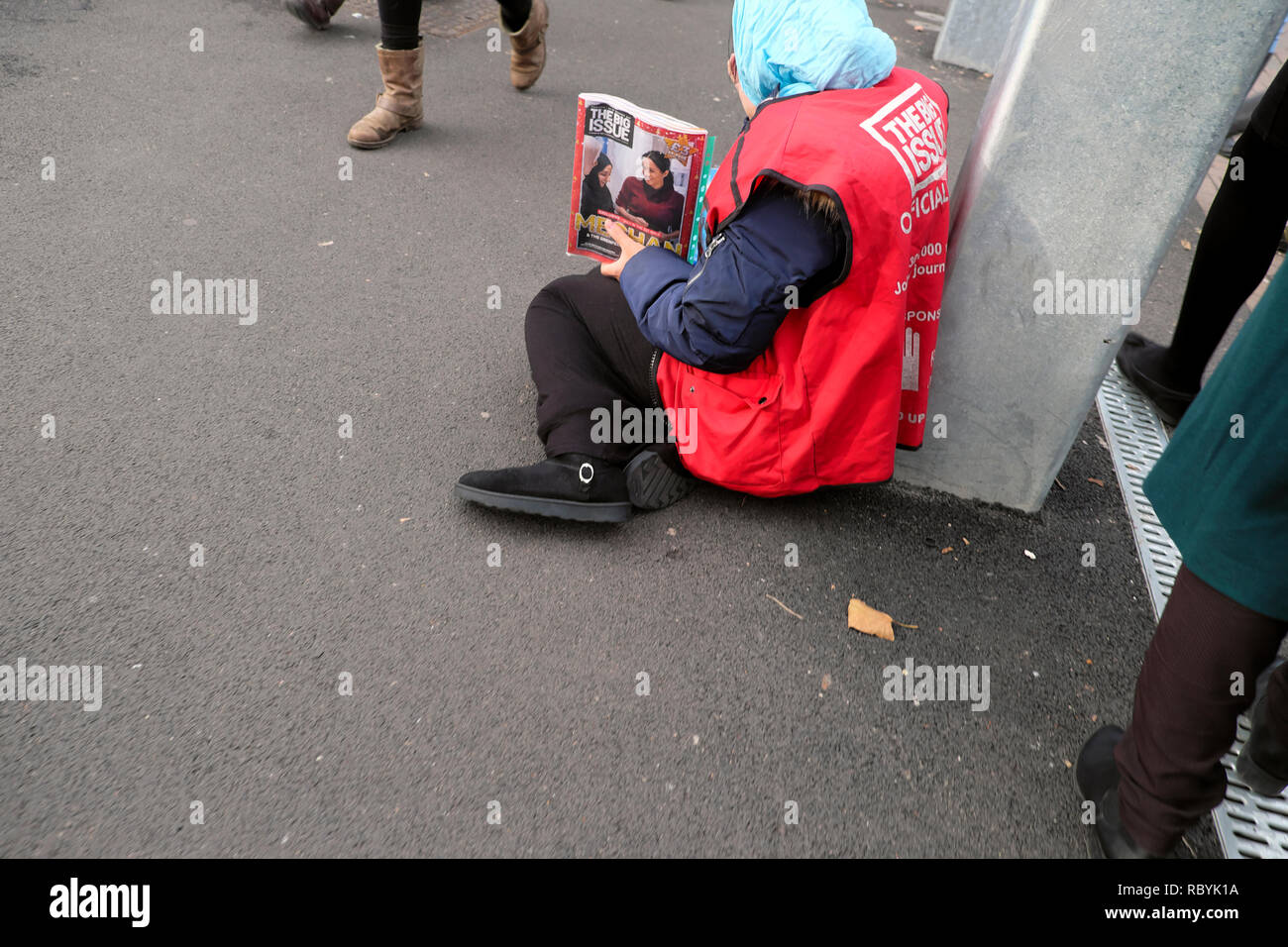 An older woman Big Issue magazine vendor sitting on the pavement selling magazines Meghan Markle on front cover in London England UK  KATHY DEWITT Stock Photo