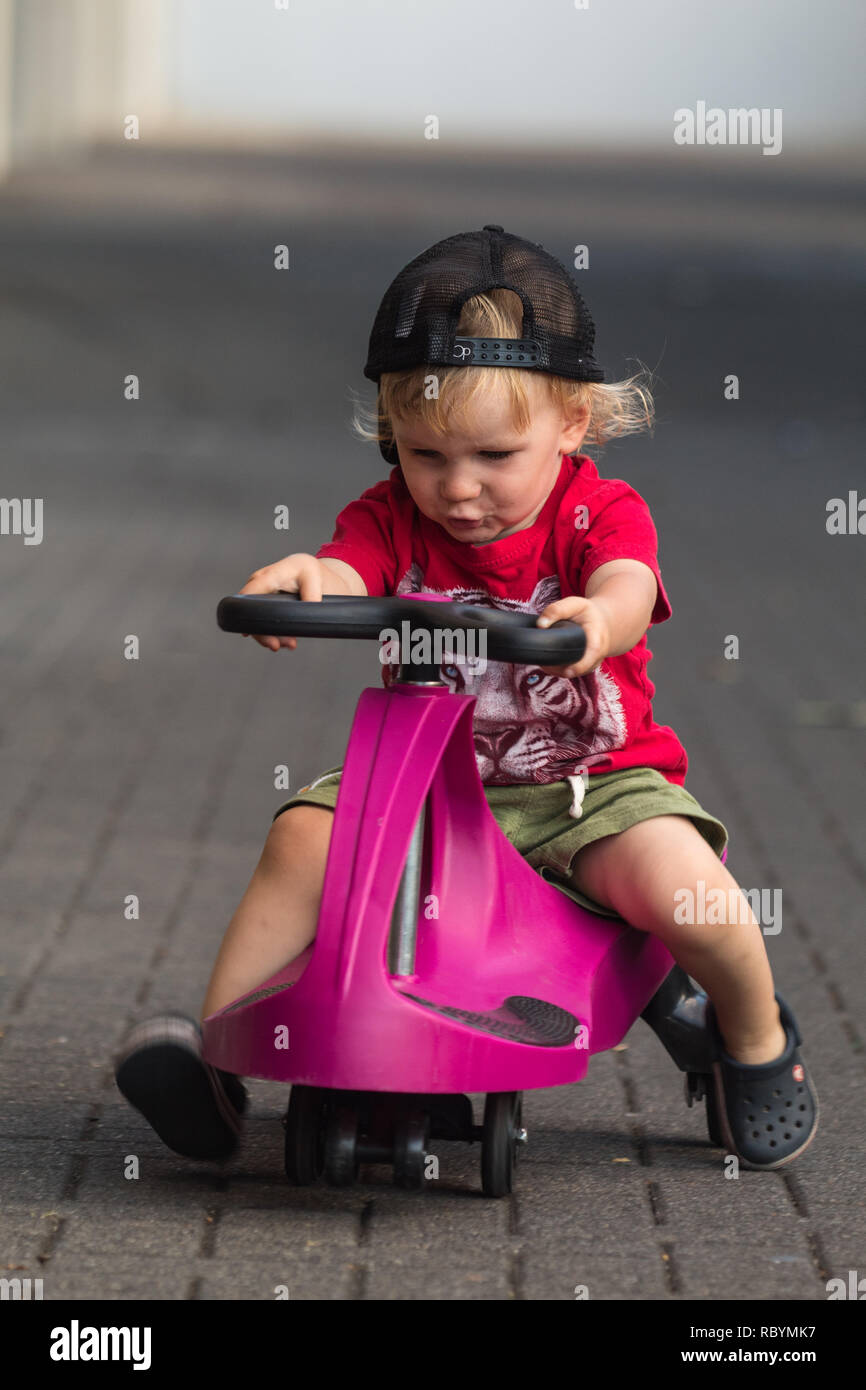 A photo of a happy kid driving with a purple plasma car like ride on toy Stock Photo