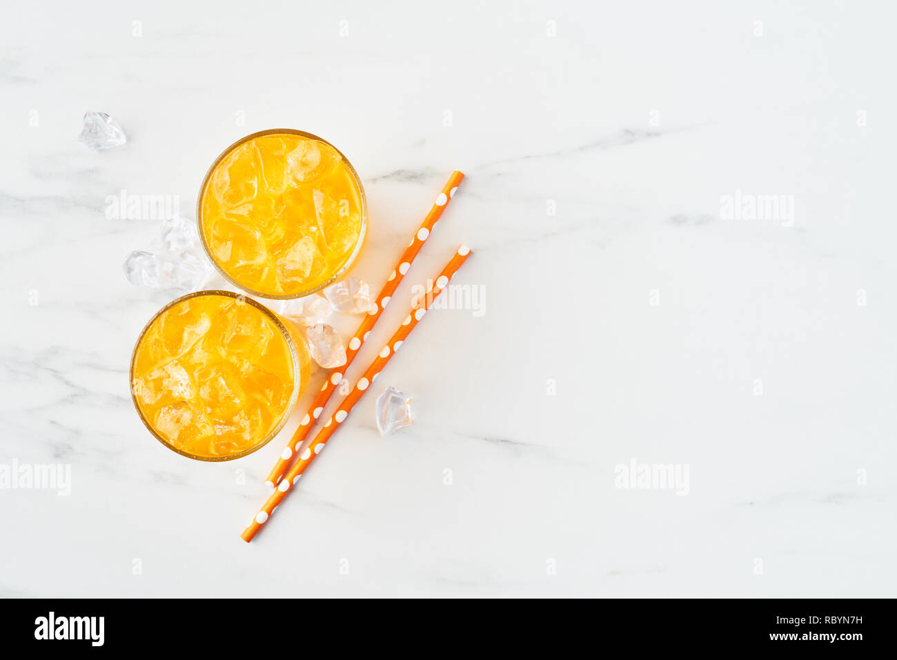 Fresh orange, mango or lemon juice in tall glass with ice and straws on white marble background. Summer drink. Top view. Copy space for text. Stock Photo