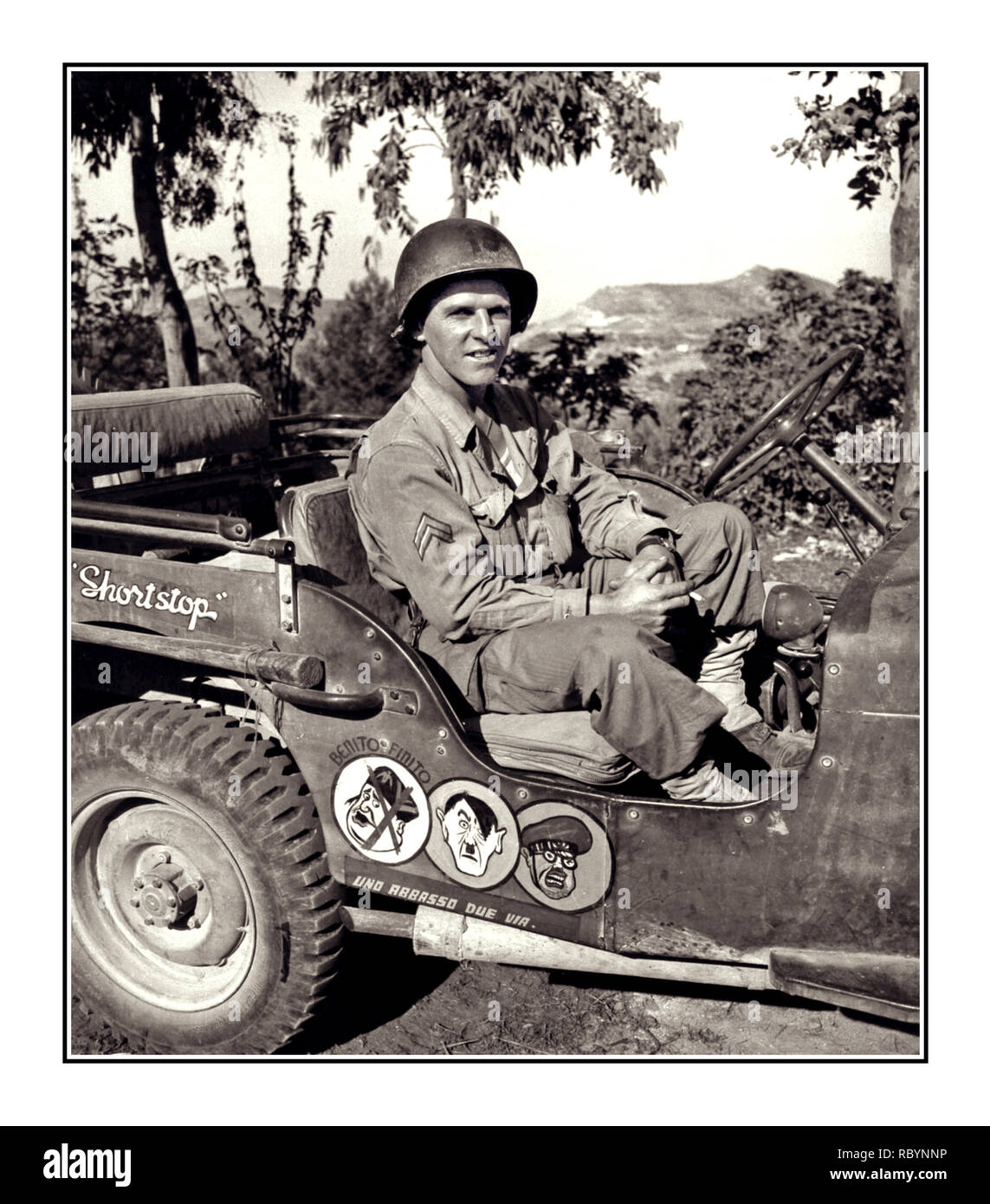WW2 ITALY Archive war humour with an American GI soldier posing in a military Jeep in Italy which has painted amusing anti Axis cartoons of leaders of Evil – Benito Mussolini, Adolf Hitler and Hideaki Tojo – Prime Minister of Japan. Stock Photo