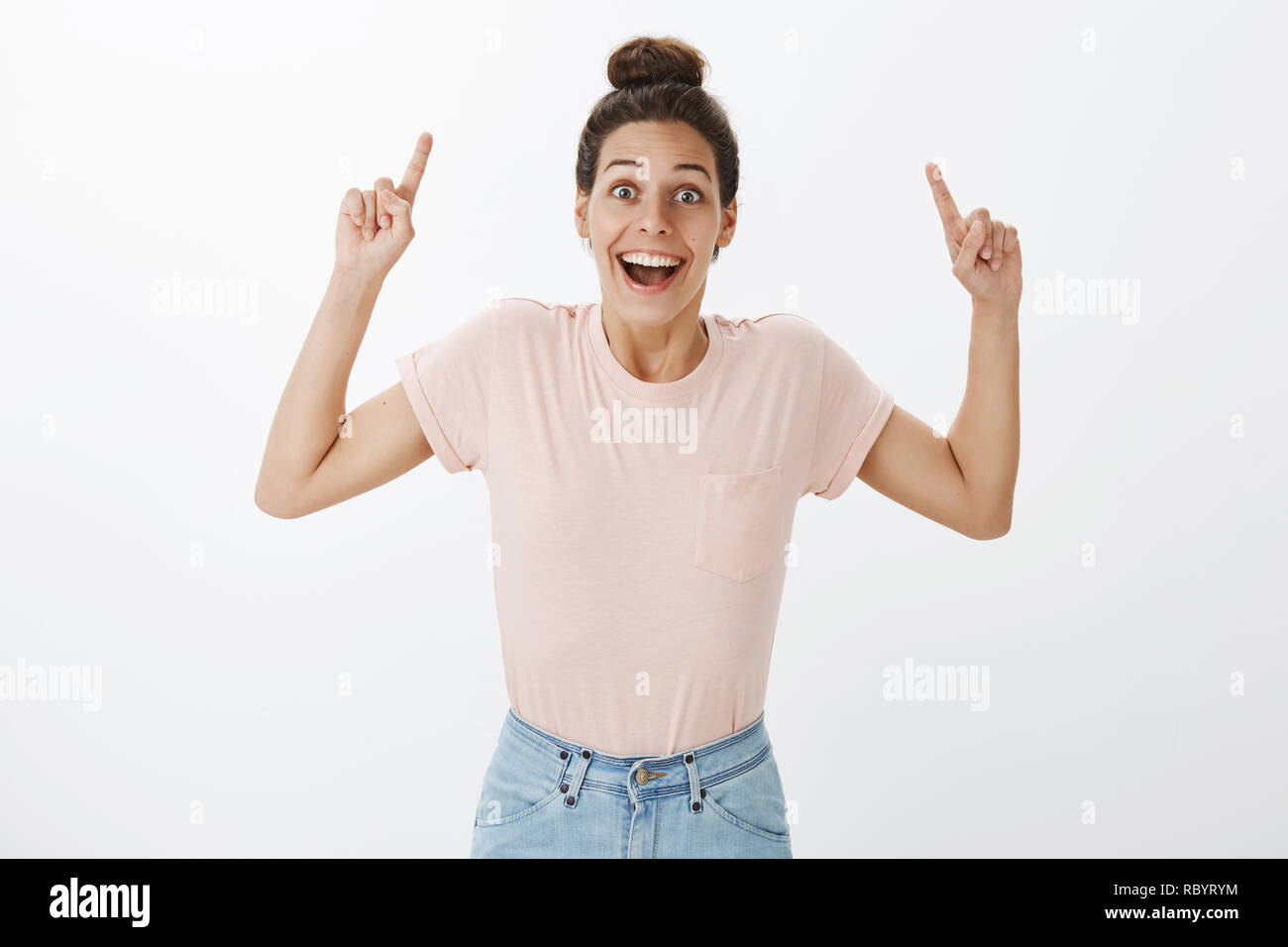 Amused delighted and optimstic good-looking caucasian girl with tan and hairbun raising index finger to point up smiling joyful and excited as showing amazing copy space over gray background Stock Photo