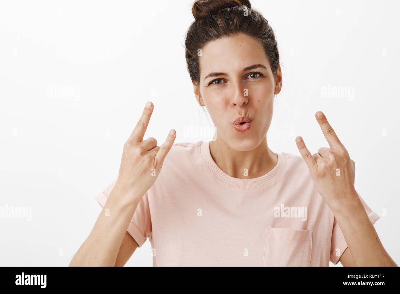 Girls rock this world. Portrait of energized and confident good-looking woman showing rock-n-roll gesture folding lips in cheer making self-assured expression as having fun at party over gray wall Stock Photo