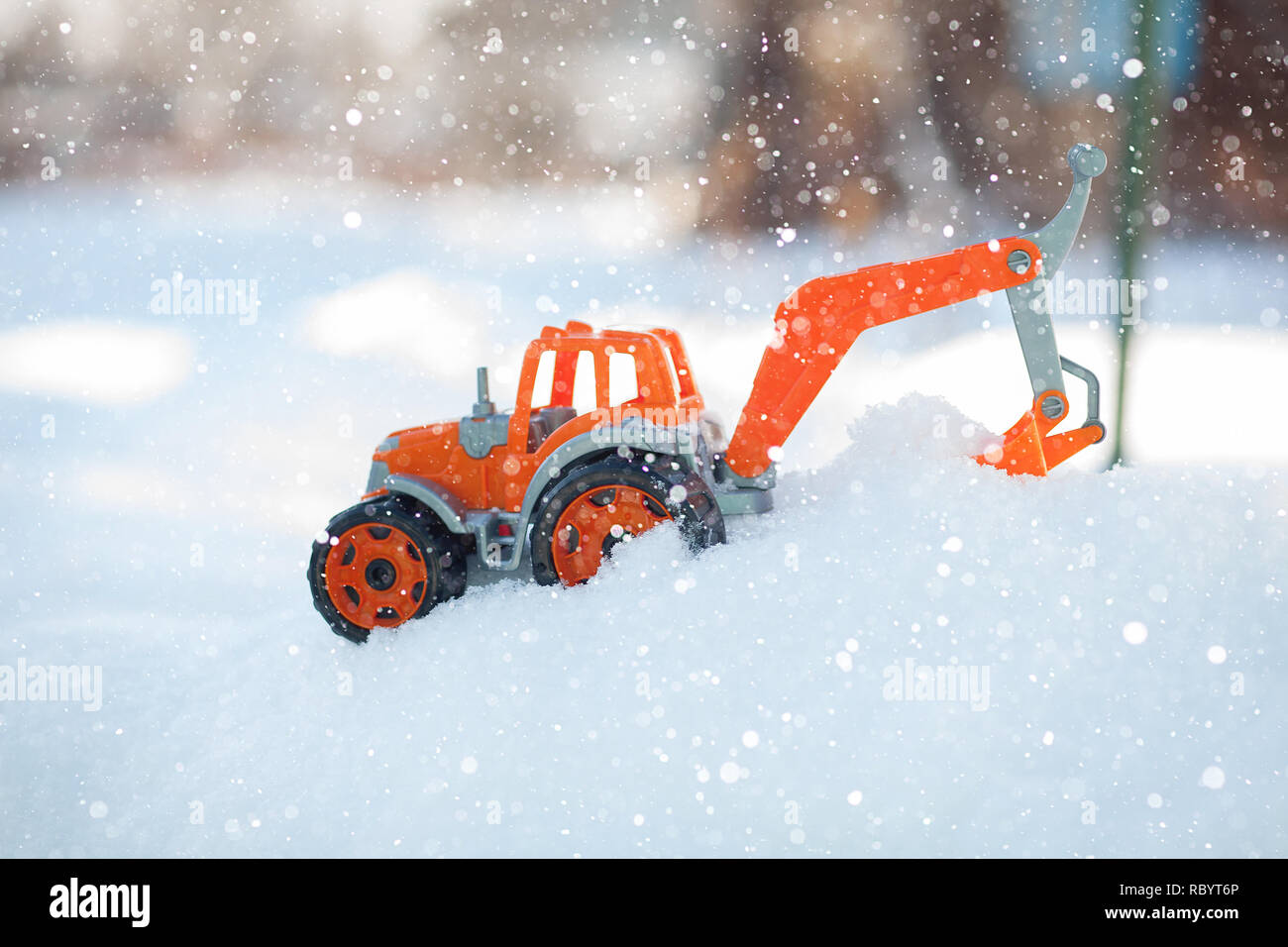Orange toy tractor with large black wheels close-up, standing in the snow. Stock Photo