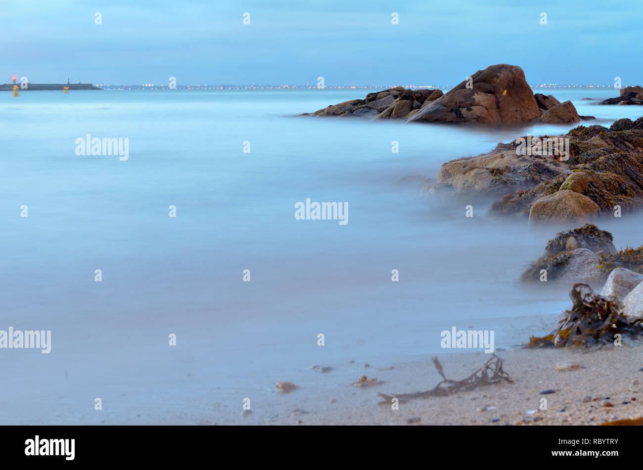 Rocky seashore,calm Irish sea at dusk,waves gently lapping onto rocks. Stock Photo