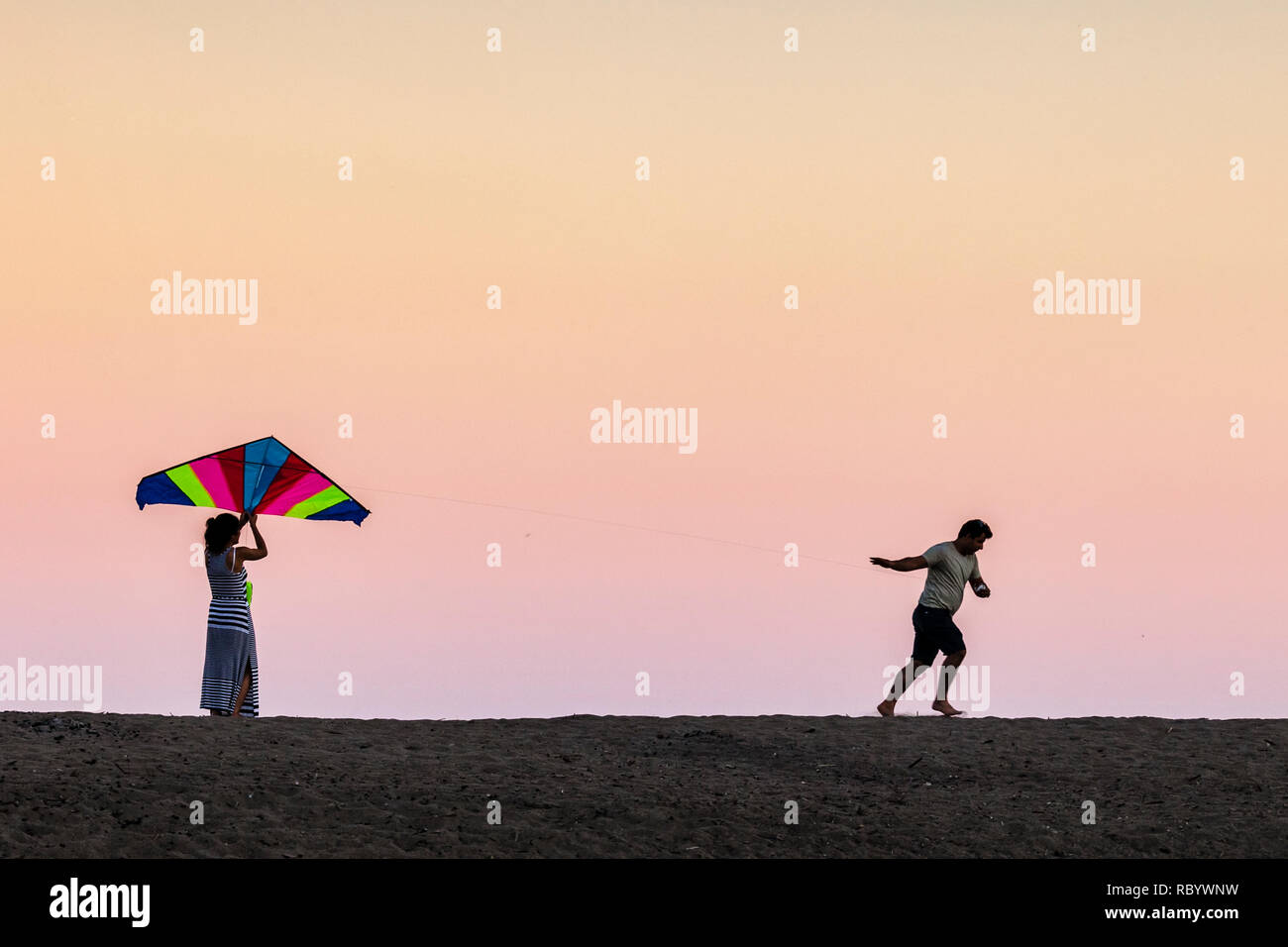 Couple on a beach flying a kite in late evening light Stock Photo - Alamy