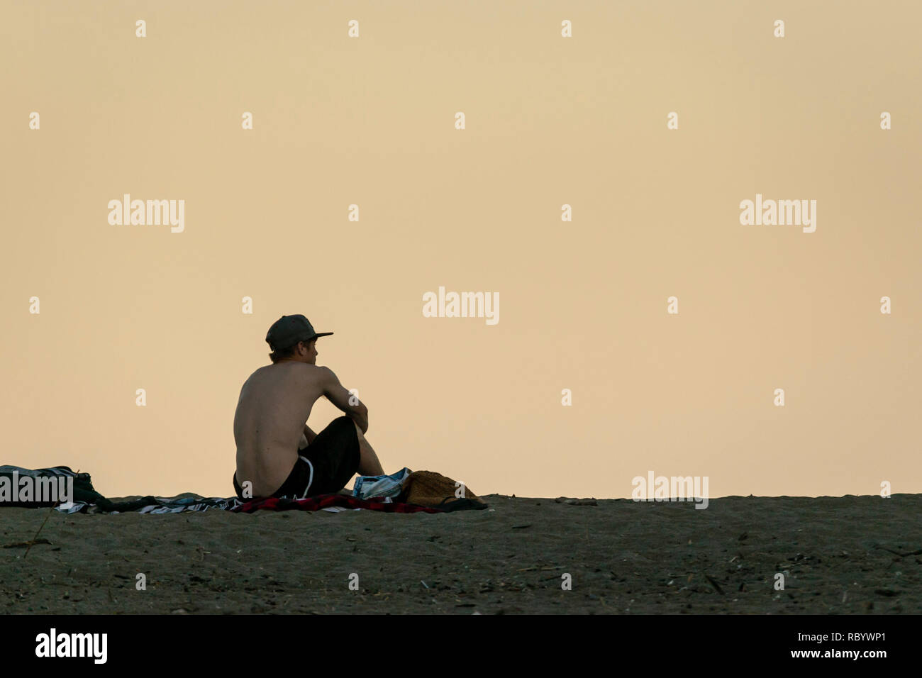 One man with cap sitting on a deserted beach. Stock Photo