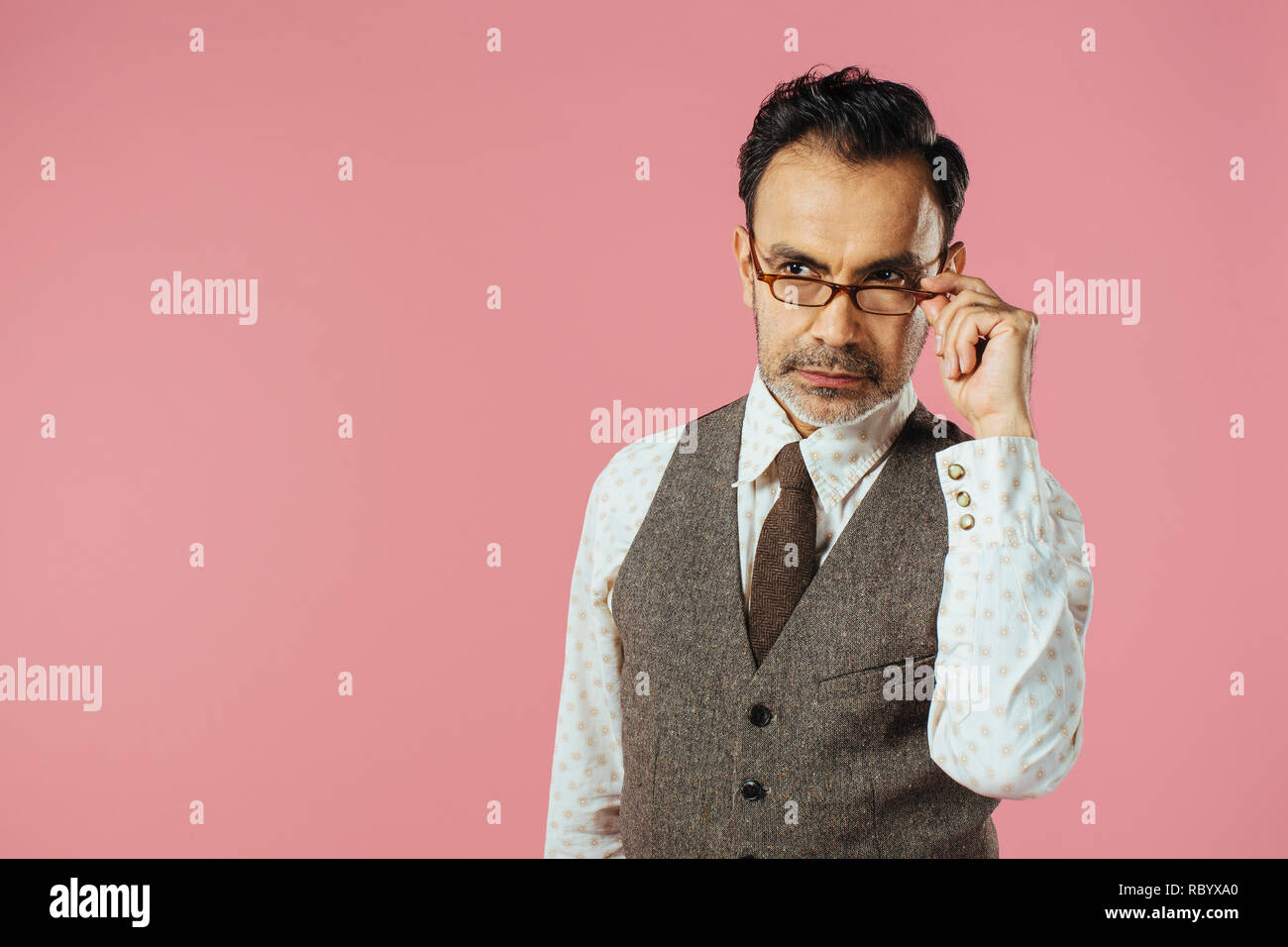 Portrait of a mature man in brown vest holding his glasses, isolated on black studio background Stock Photo