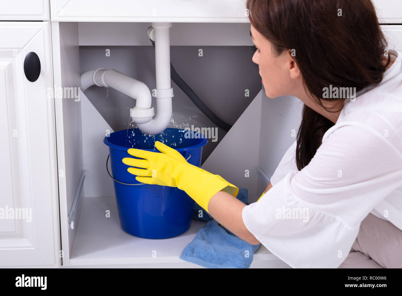 Closeup Of A Young Woman Placing Blue Bucket Under Water Leaking From