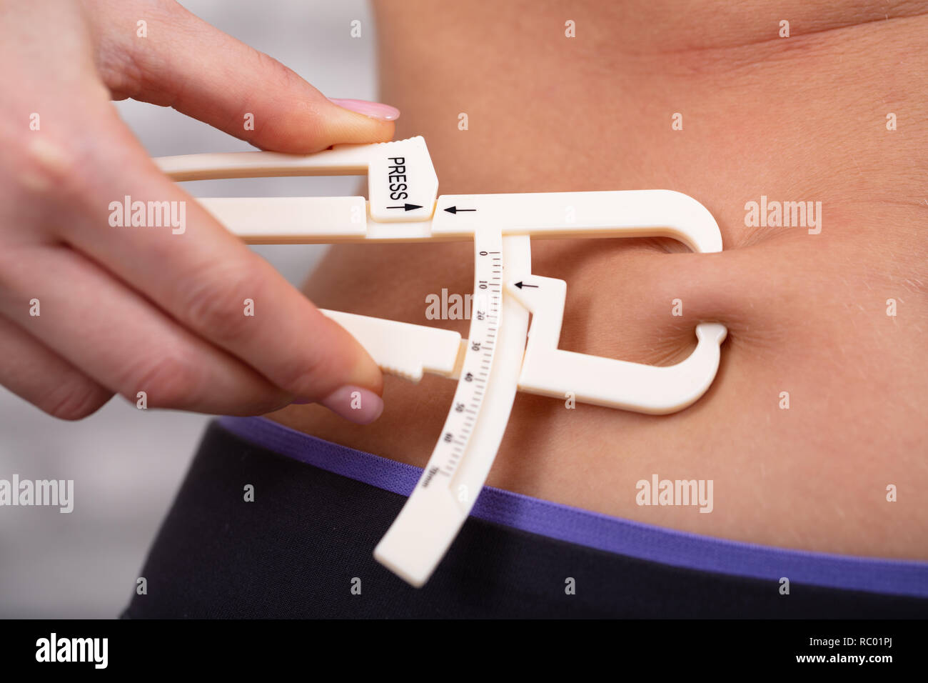 Body fat calipers, woman measuring subcutaneous percentage of fat on her  belly. Young woman using skinfold calipers Stock Photo - Alamy