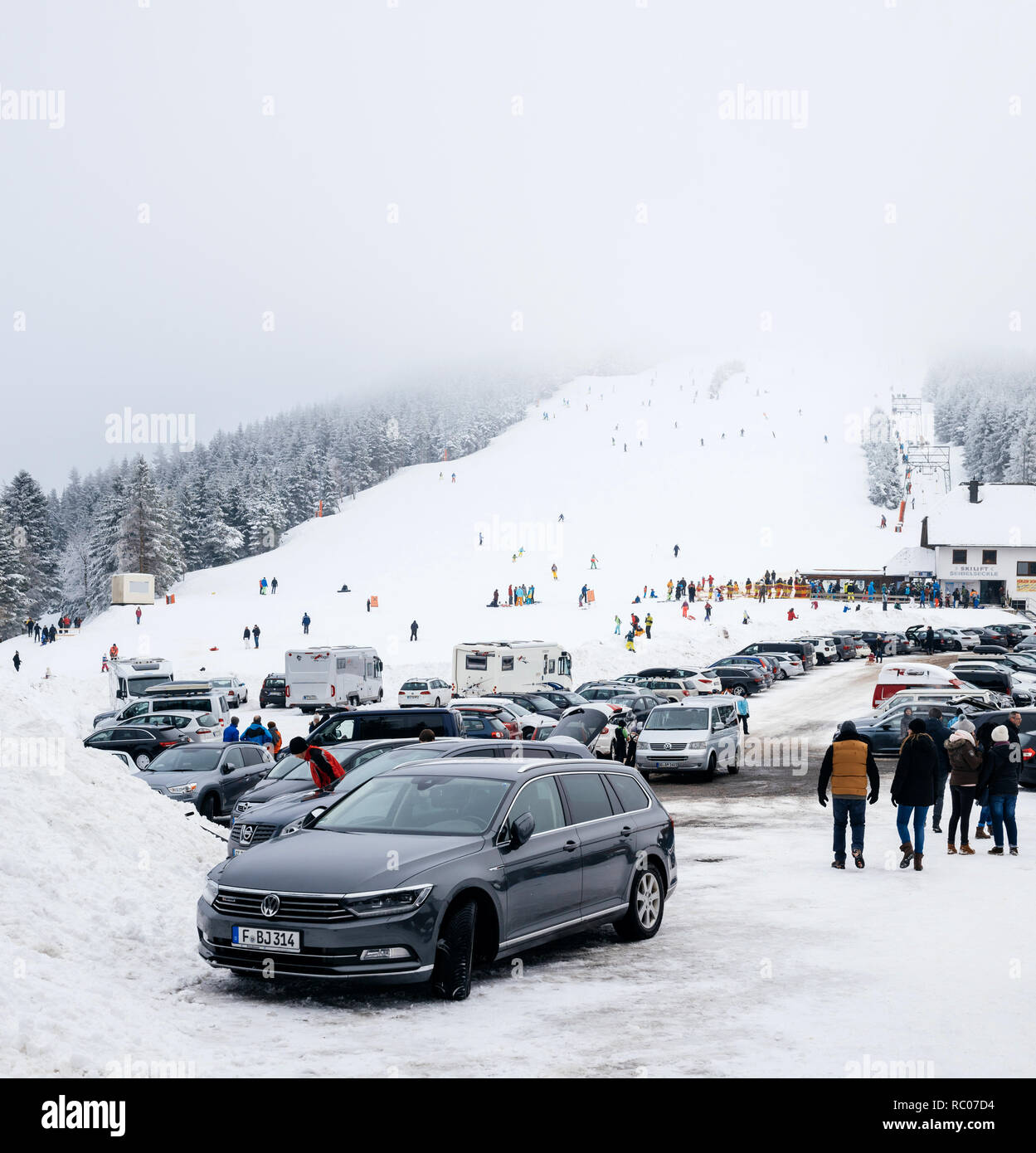 MUMMELSEE, GERMANY - FEB 18, 2018: Winter day with snow and ski slope seen from parking area with kids, parents having fun in German mountains and Volkswagen Passat estate car parked Stock Photo