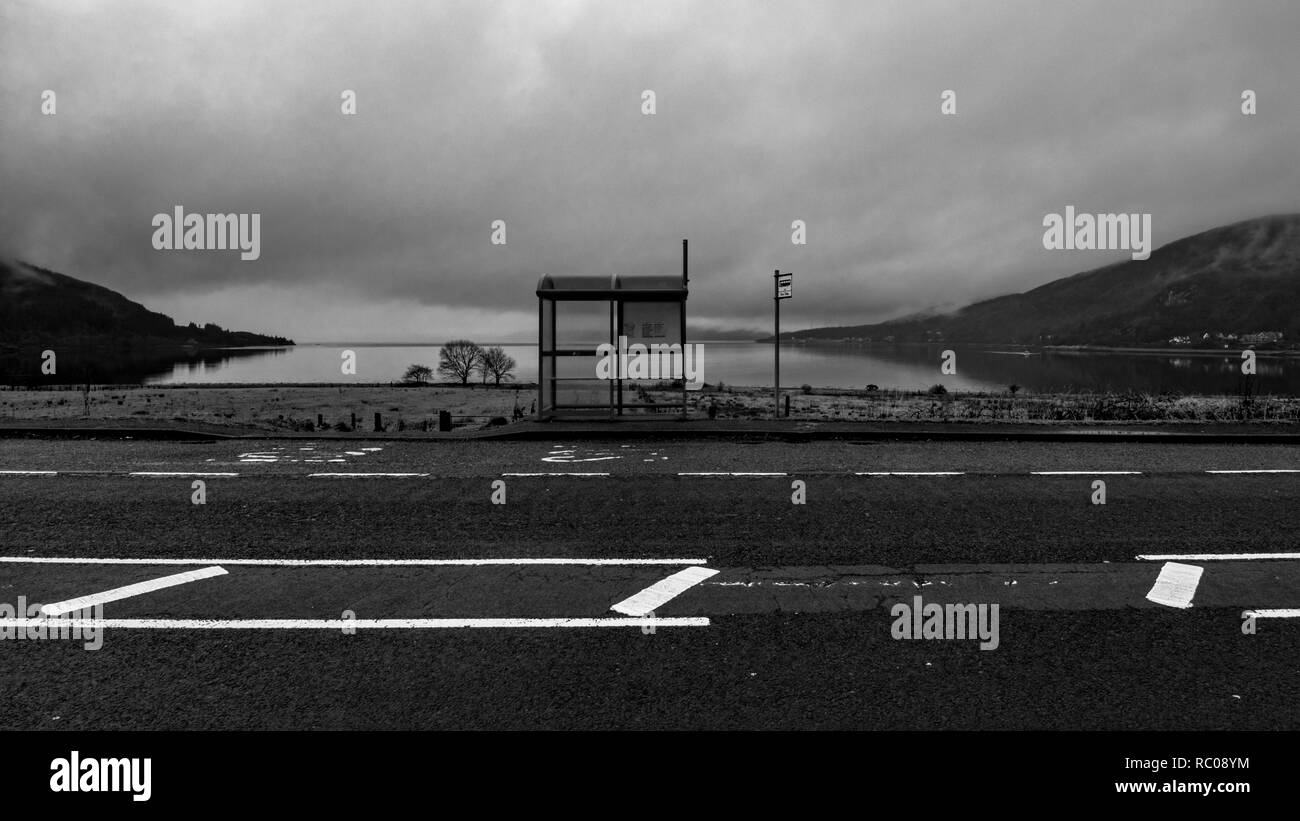 Black and white picture of the bus stop in country side area up North in Scotland near Fort William. Empty road and lake on the background Stock Photo