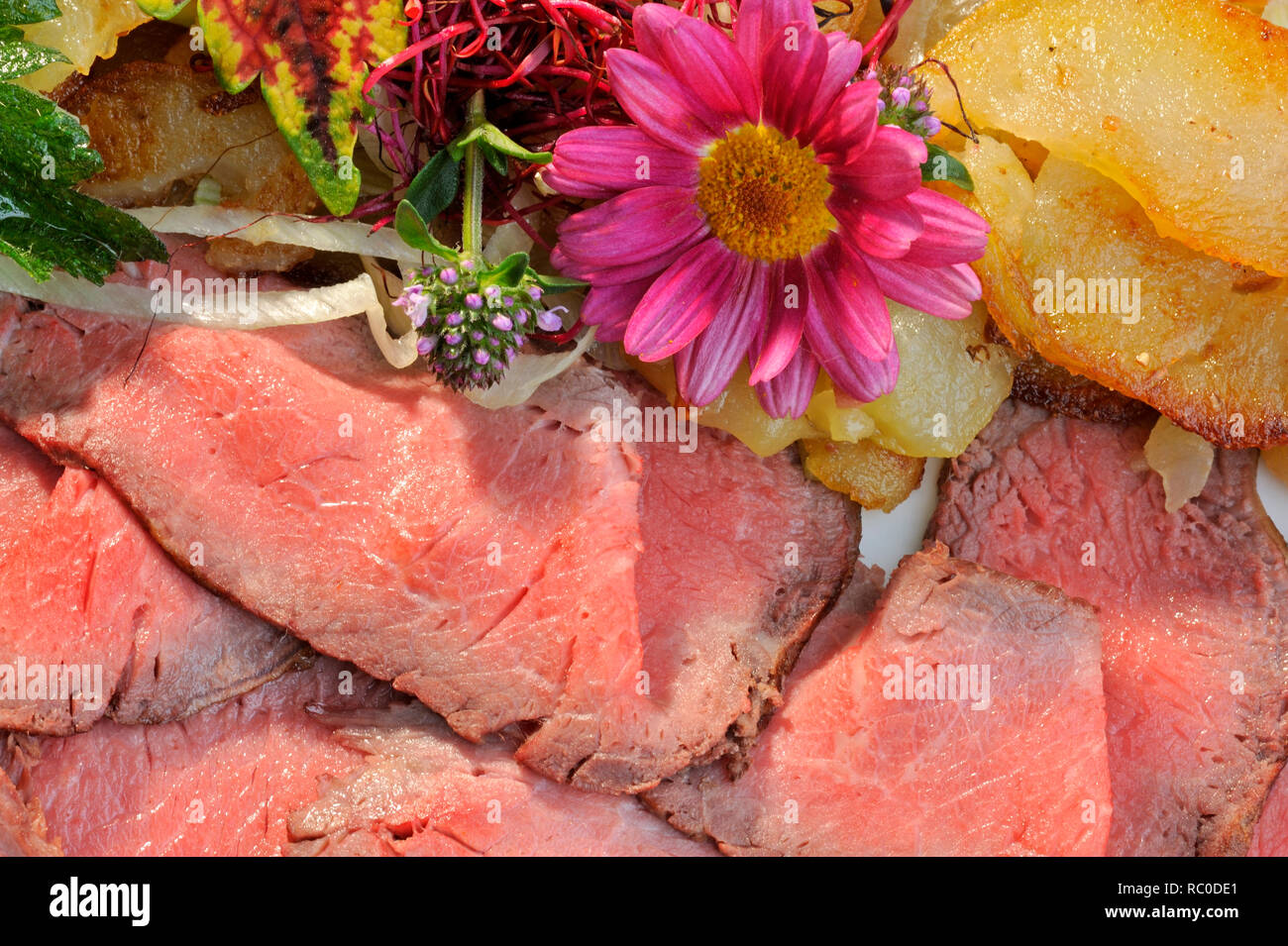 Roastbeef mit Bratkartoffeln, dekoriert mit essbaren Blüten und Kräutern | roast beef with roast or fried potatoes Stock Photo