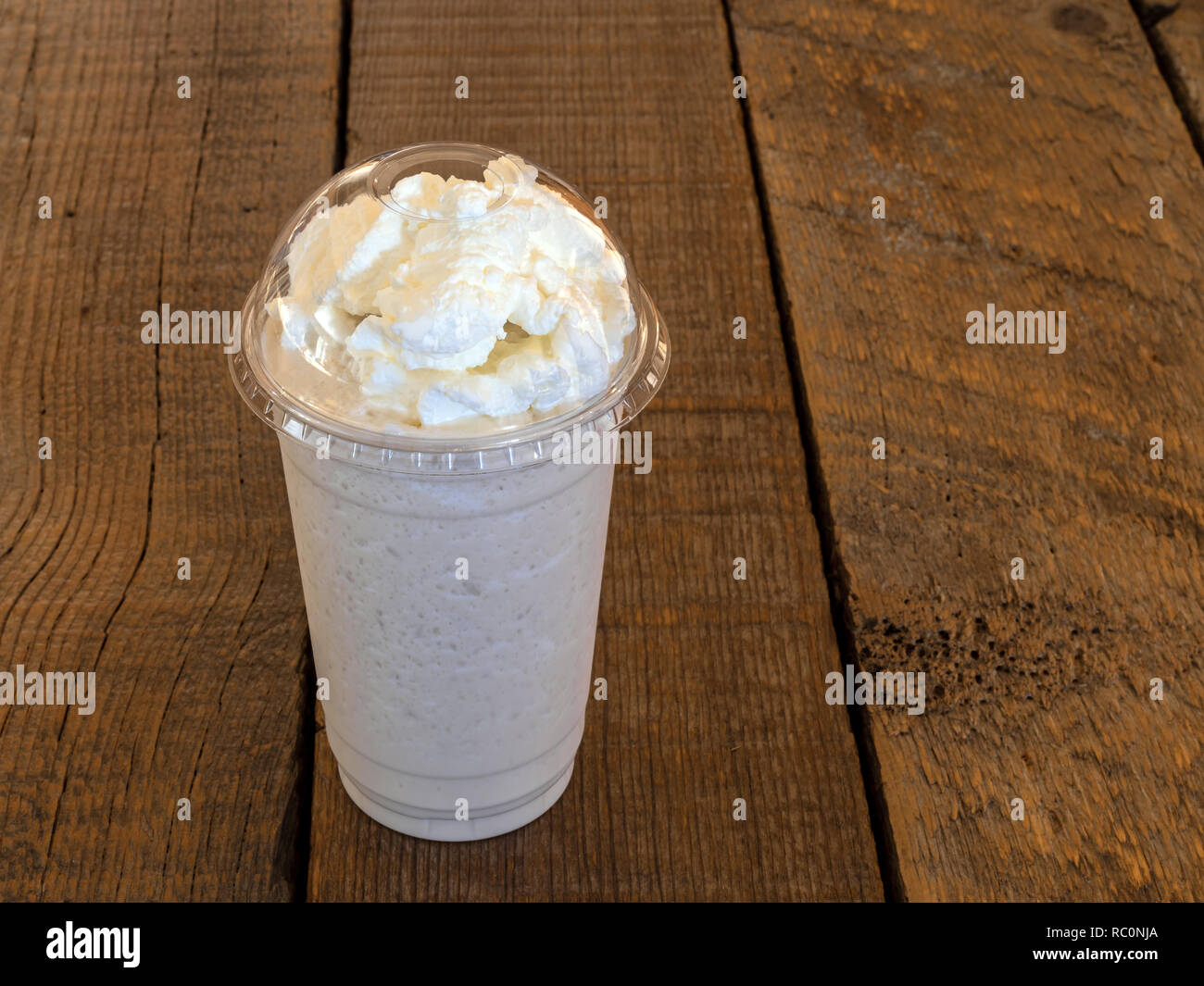 Vanilla Frappe coffee drink in a clear cup with whipped cream on top on a barn wood background with copy space. Stock Photo